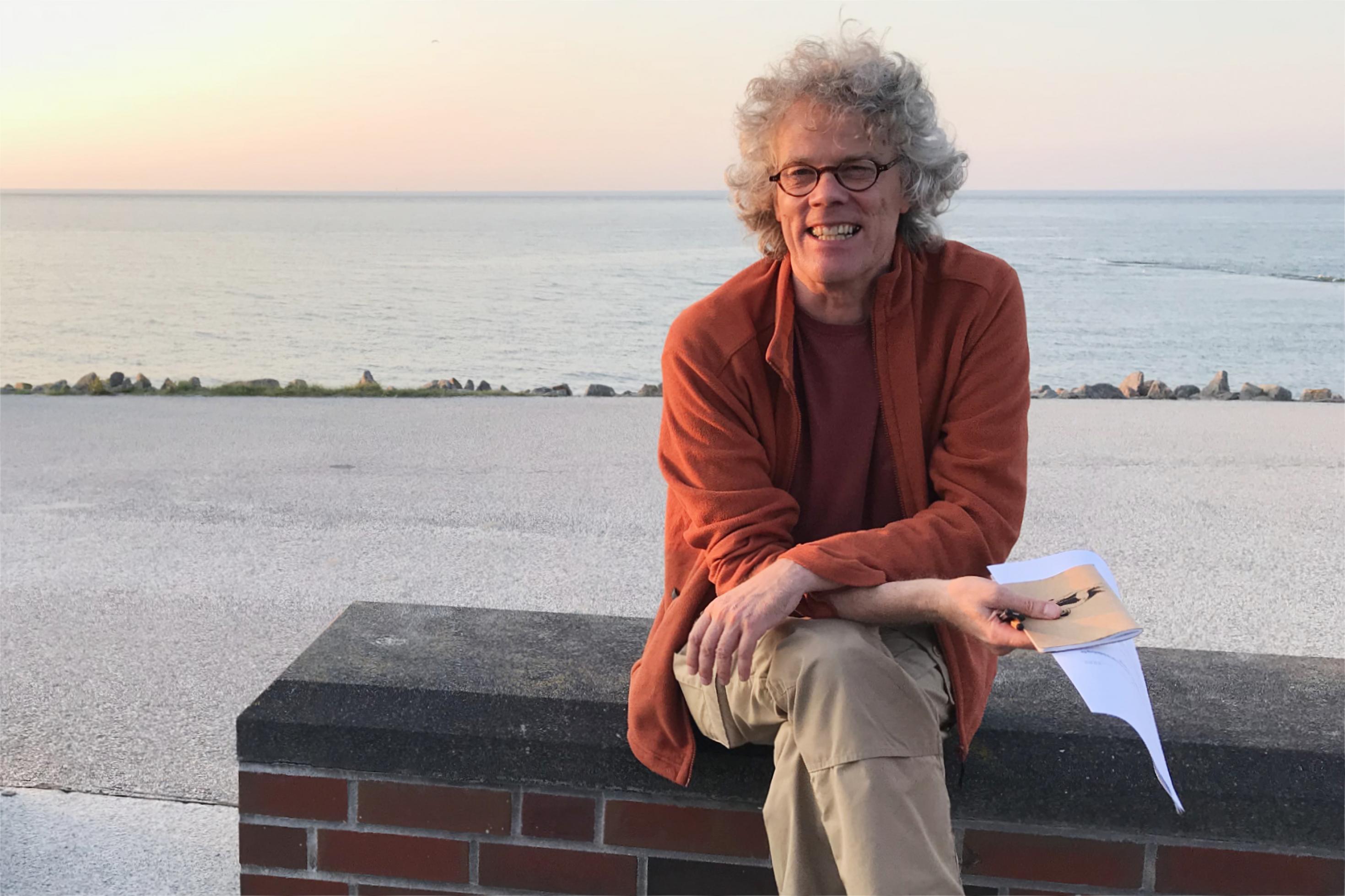 Reno Lottmann sitzt im Abendlicht auf einem Steinblock an der Promenade von Baltrum.