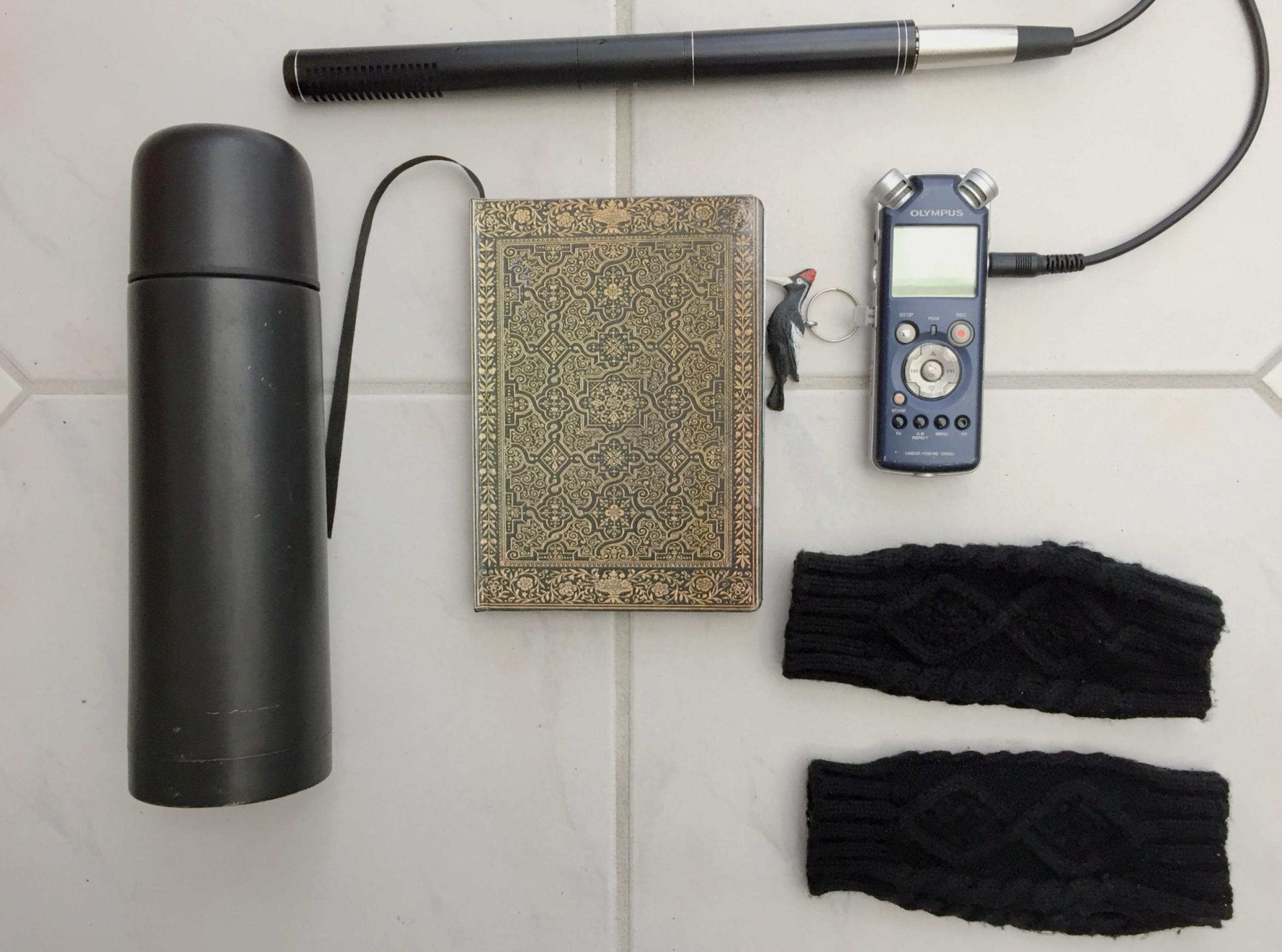 Notizbuch, Glückbringer, Thermoskanne, Mikrofon mit Aufnahmegerät und Pulswärmer