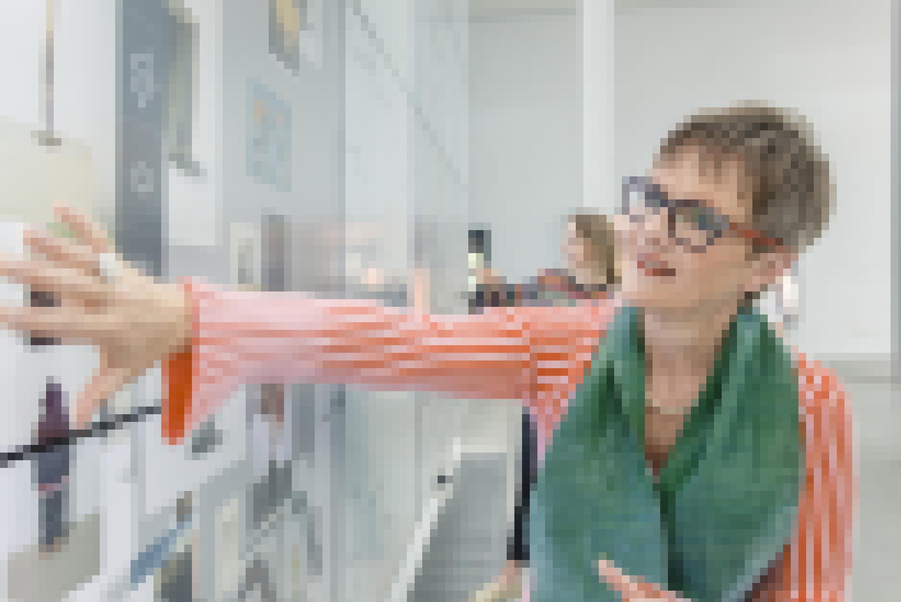 Eine Frau mit auffälliger Brille und grünem Schal bedient einen riesigen, an der Wand hängenden Touchscreen.