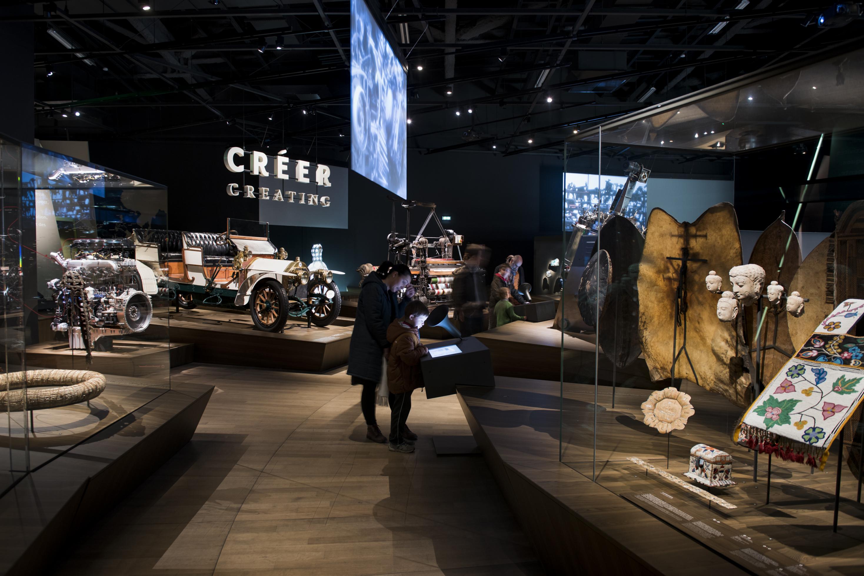 Ein Ausstellungsraum mit unterschiedlichen Exponaten wie Schutzschilde aus Afrika, ein frühes Automobil, ein Webstuhl.