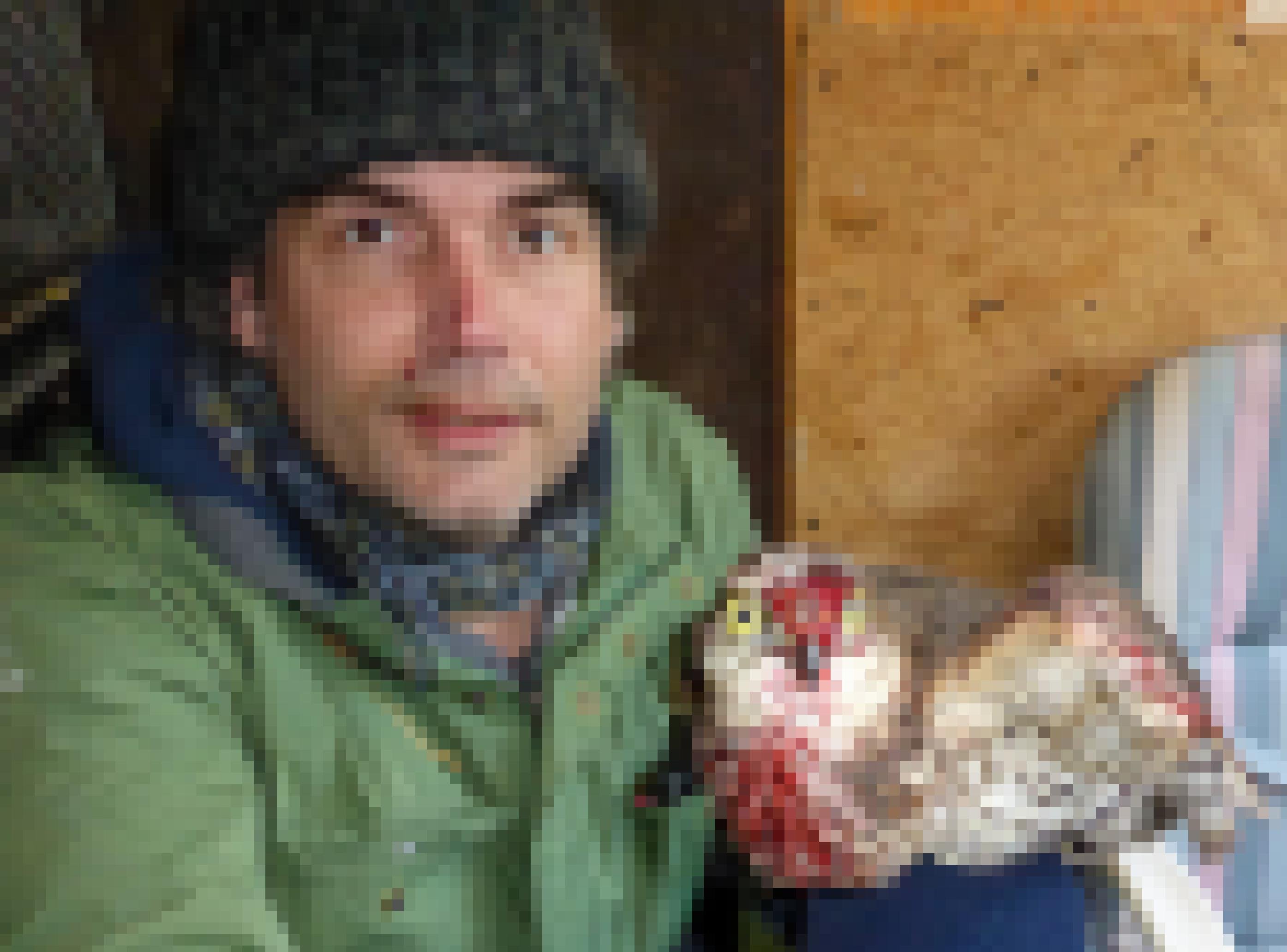Ein Mann mit Wollmütze präsentiert einen Greifvogel, dessen Schnabel und Brust blutverklebt sind.