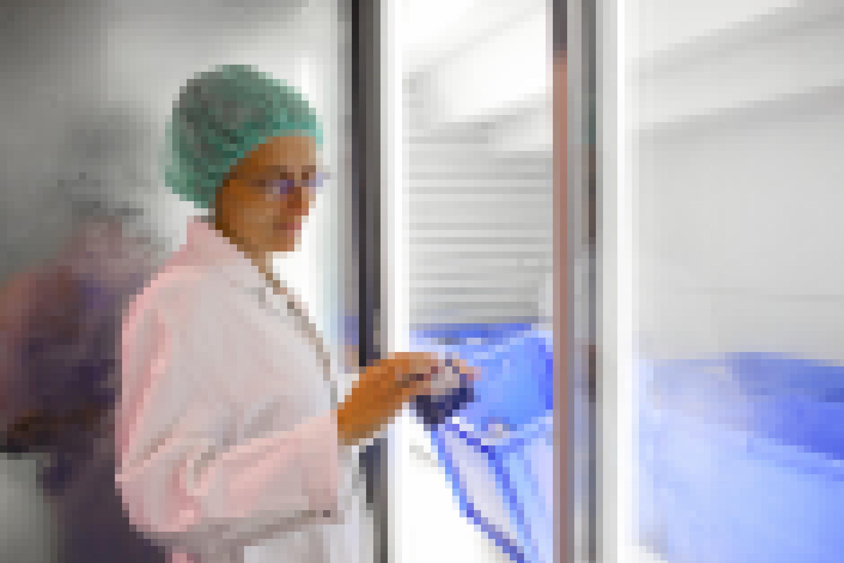 Das Bild zeigt eine Frau in medizinischer Schutzkleidungsamt Haube in einer sterilen Umgebung. Sie hält eine kleine Schachtel in der Hand, in der sich ein medizinischer Test befindet.