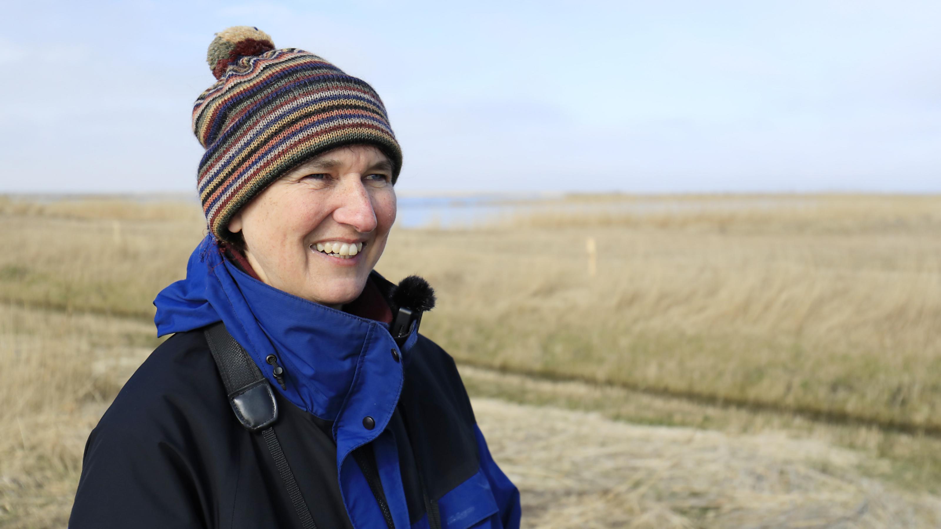 Barbara Ganter steht in blau-schwarzer Winterjacke und Mütze vor einer Graslandschaft.