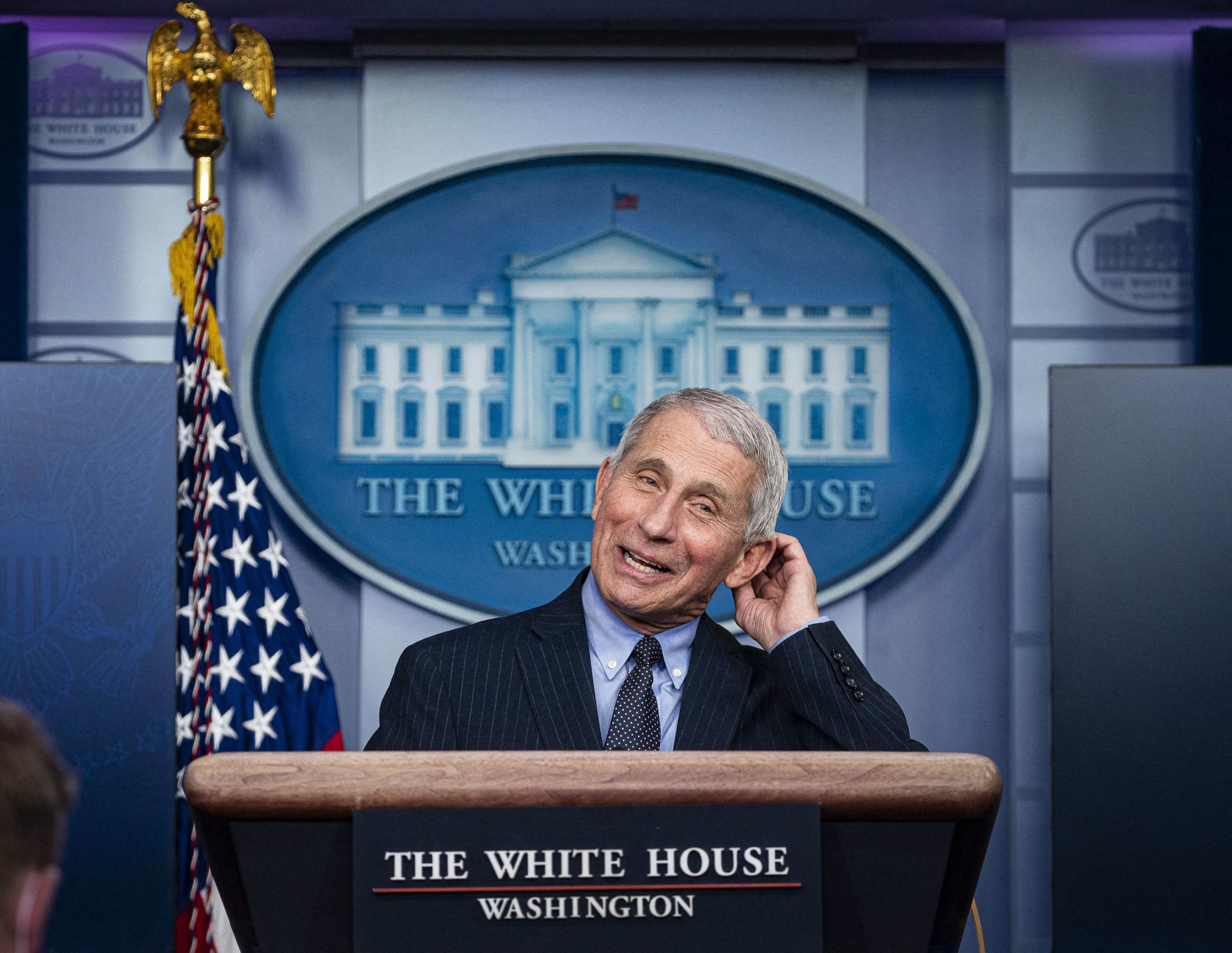 Ein grauhaariger Mann in schwarzem Anzug, blauem Hemd und Krawatte steht hinter einem Pult mit der Aufschrift „The White House“. Im Hintergrund das Logo des Weißen Hauses und eine amerikanische Fahne an einer Stande, die von einem goldenen Adler gekrönt ist.
