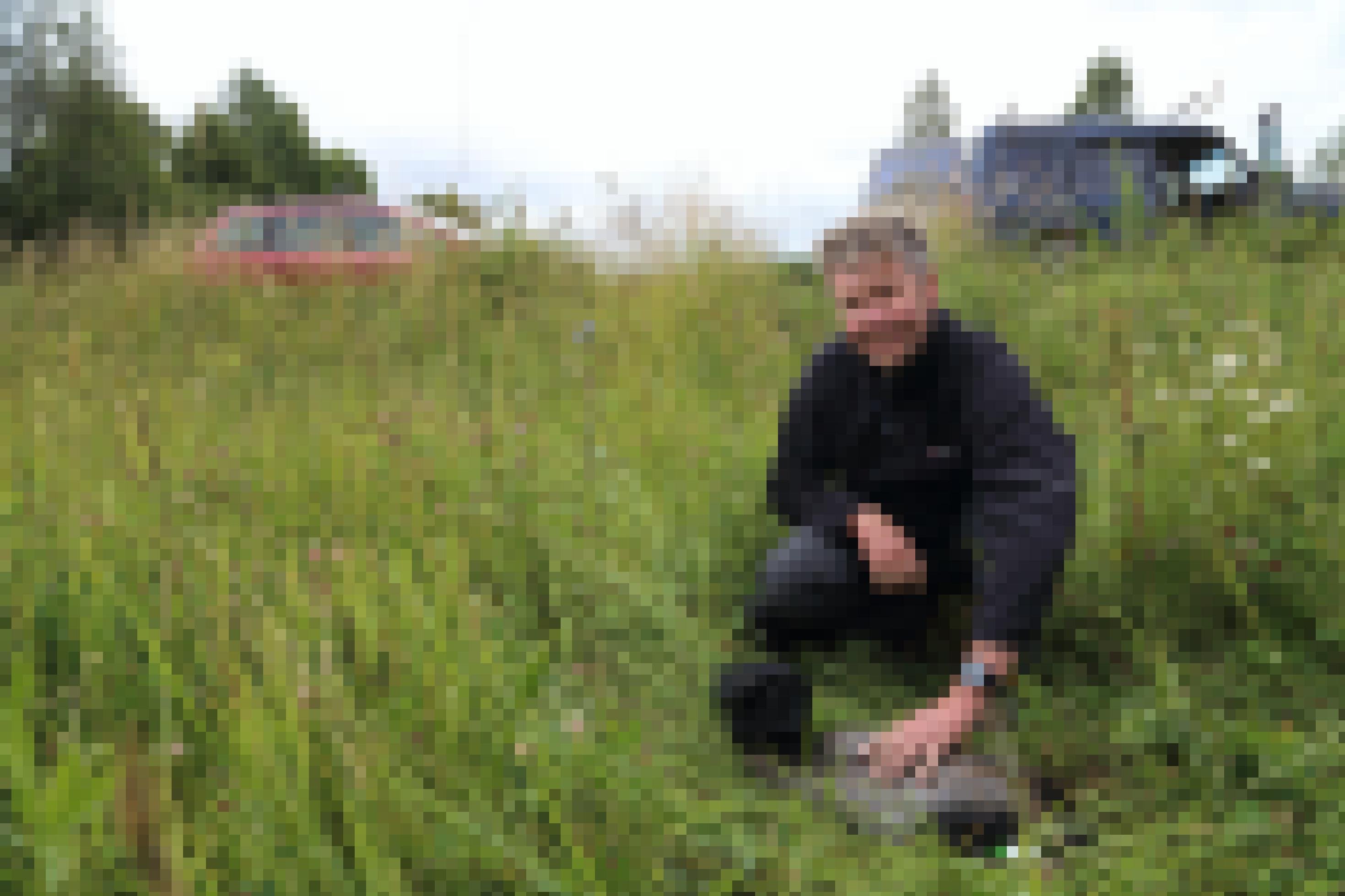 Der Biologe Günter Nowald, vor ihm in der Wiese liegt ein Kranich, der bunte Farbringe trägt.