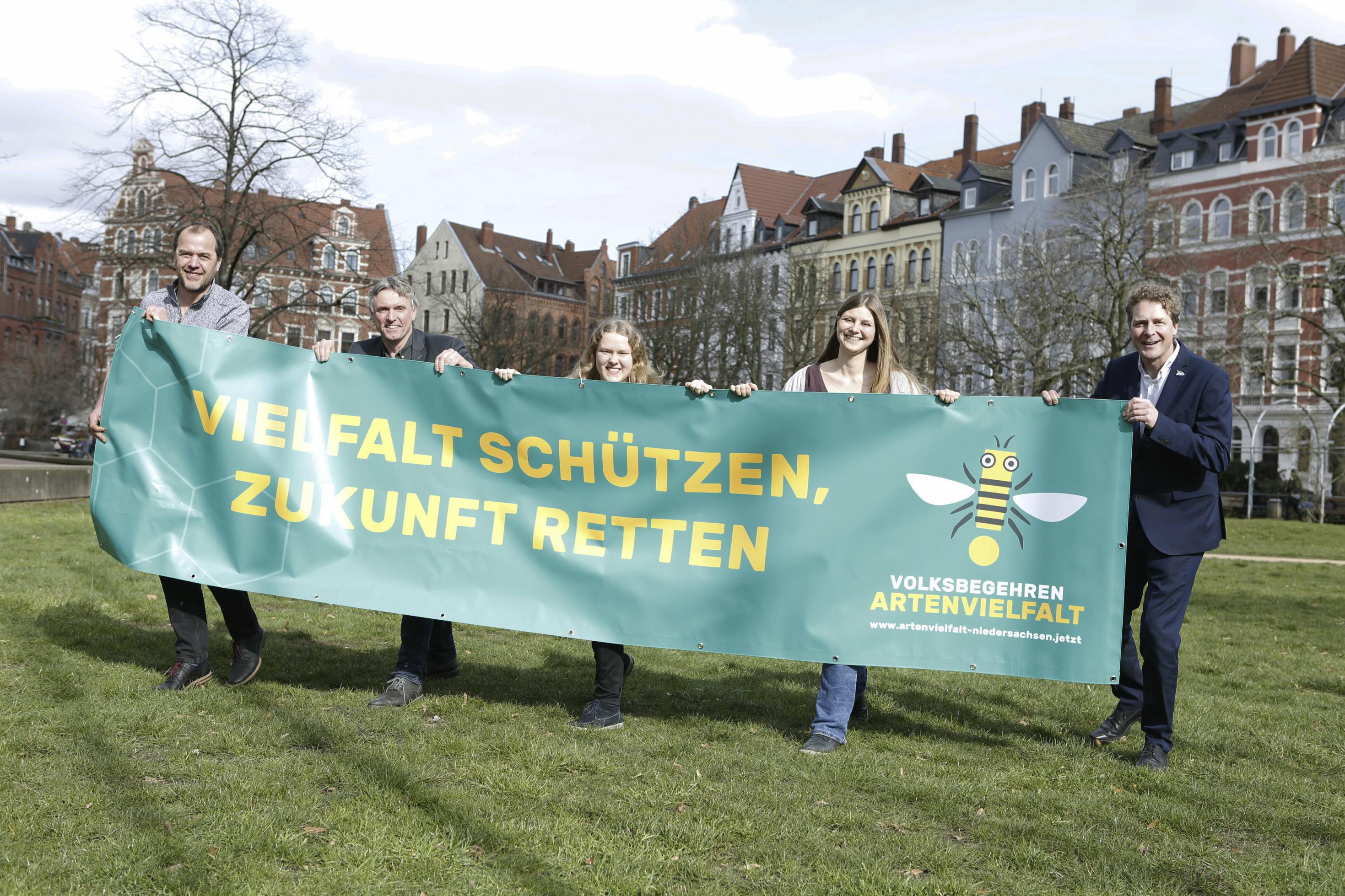 Zwei Frauen und drei Männer stehen auf einer Wiese und halten ein Transparent vor sich mit der Aufschrift „Vielfalt schützen, Zukunft retten. Volksbegehren Artenvielfalt“ und eine stilisierte Honigbiene.