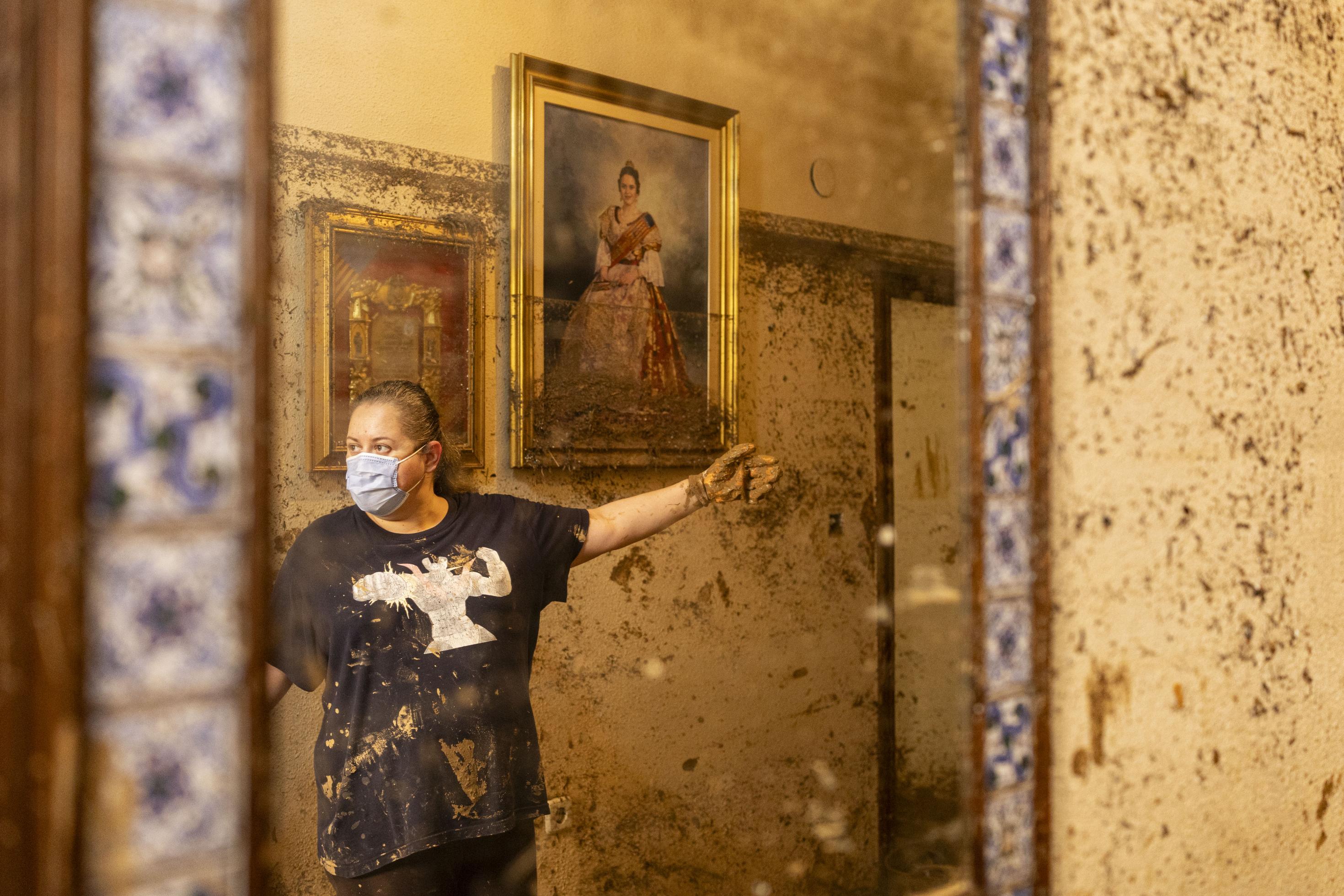 Eine Frau weist ins Innere einer Wohnung. Wie hoch die Fluten standen, ist an den Schlammspuren auf den Bildern an der Wand erkennbar.