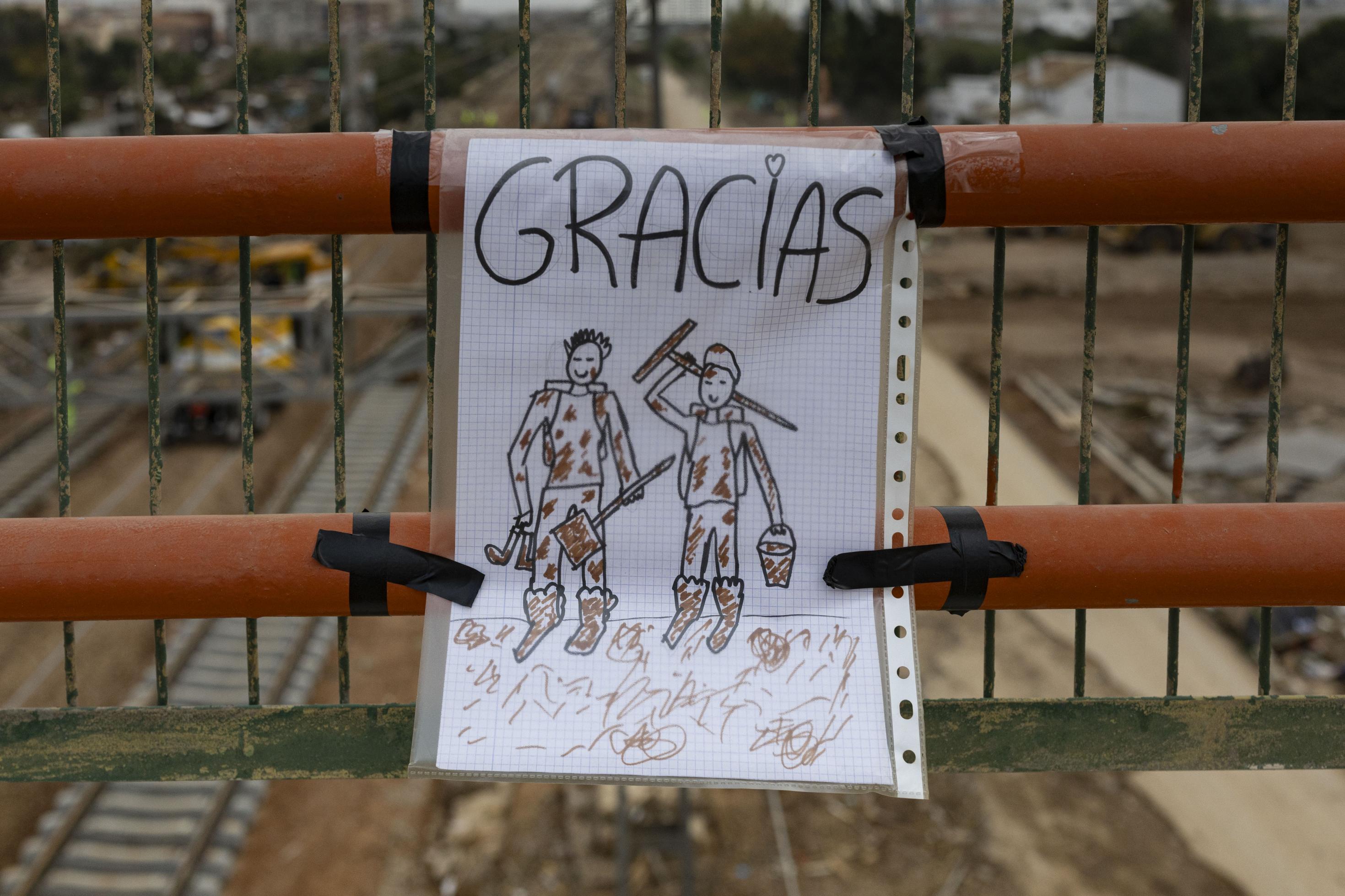 Kinder haben diese Zeichnung in eine Plastikfolie gesteckt befestigt. Über den schlammverschmierten Arbeitern steht „Danke“. Im Hintergrund sind die teils bereits reparierten Bahngleise in Richtung der Stadt Valencia zu sehen. Die Region ist eines der Logistikzentren des Landes. Unter Hochdruck arbeitet das Transportministerium an der Instand-Setzung der Infrastrukturen. Die Schäden an Straßen, Schienen, Versorgungsnetzen belaufen sich auf mindesten 4,1 Milliarden Euro.