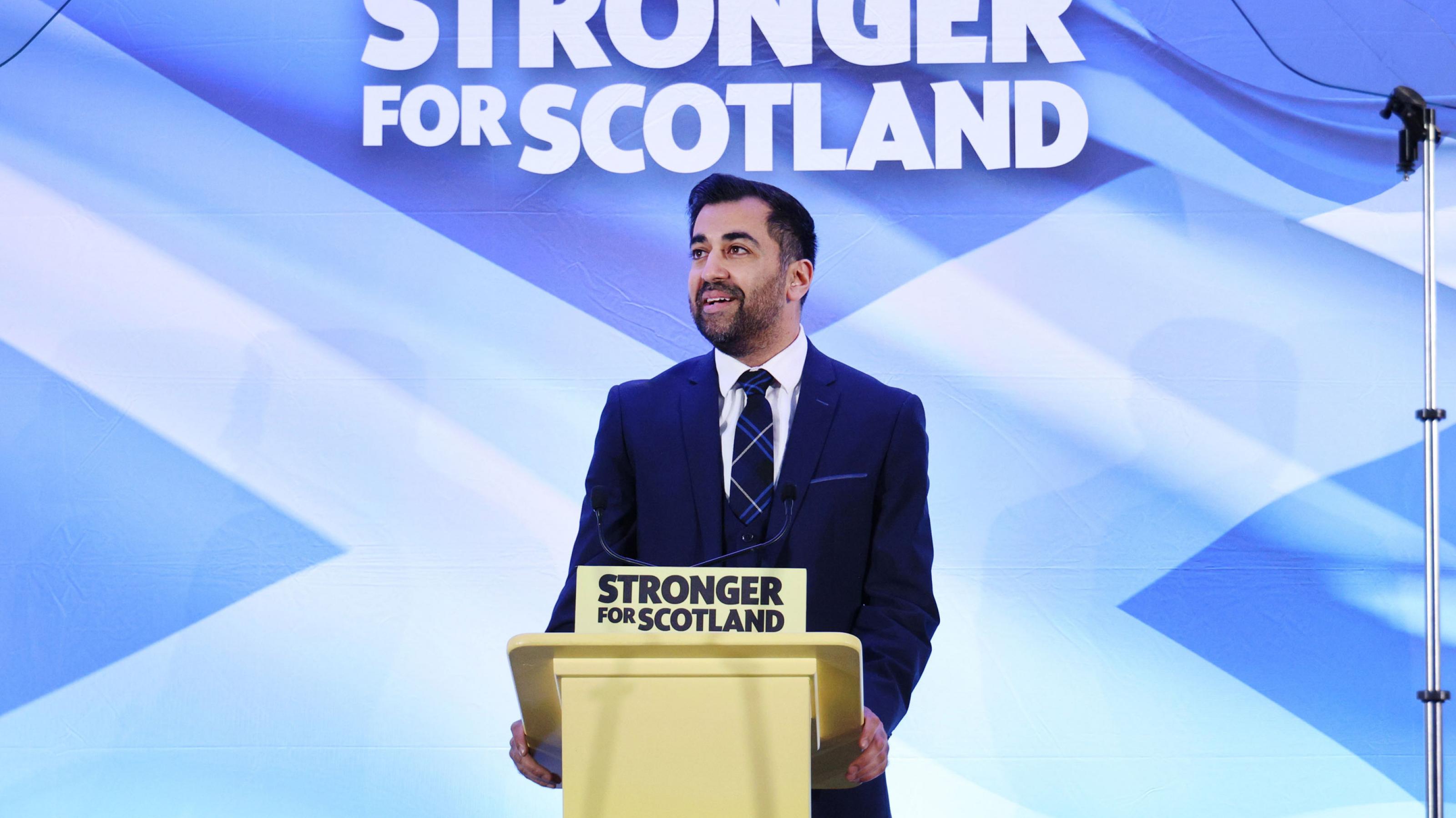 Ein Mann steht vor einem Plakat, auf dem steht: 'Stronger for Scotland'