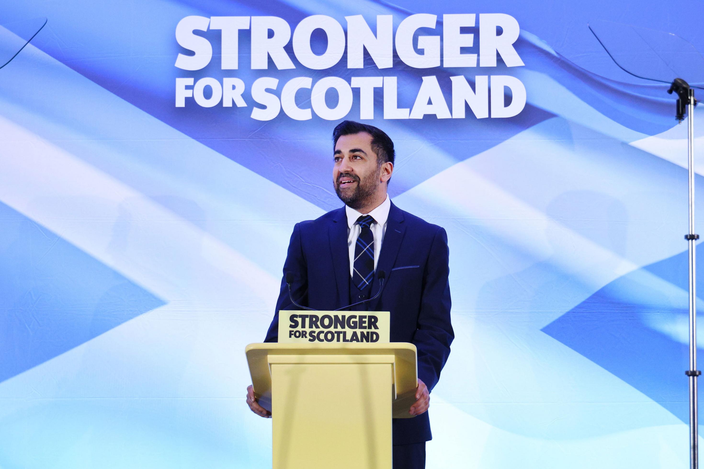 Ein Mann steht vor einem Plakat, auf dem steht: 'Stronger for Scotland'