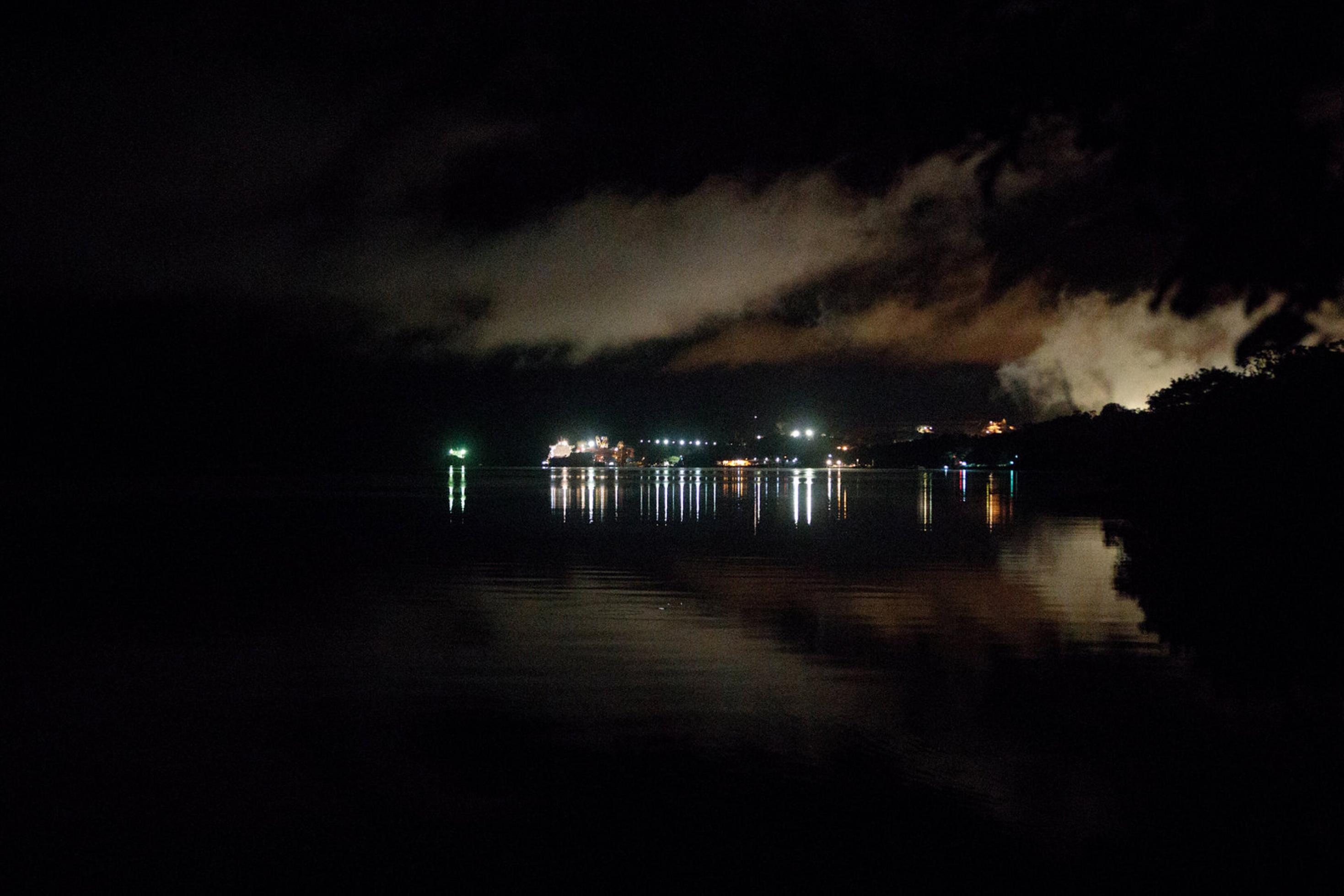 Eine Totale zeigt die dunklen Morgenstunden: Blick auf Porto Trompetas von der Gemeinde Boa Vista aus. Während die Gemeinde keinen Strom hat, erzeugt Porto Trombetas nachts einen starken Lichtpunkt.