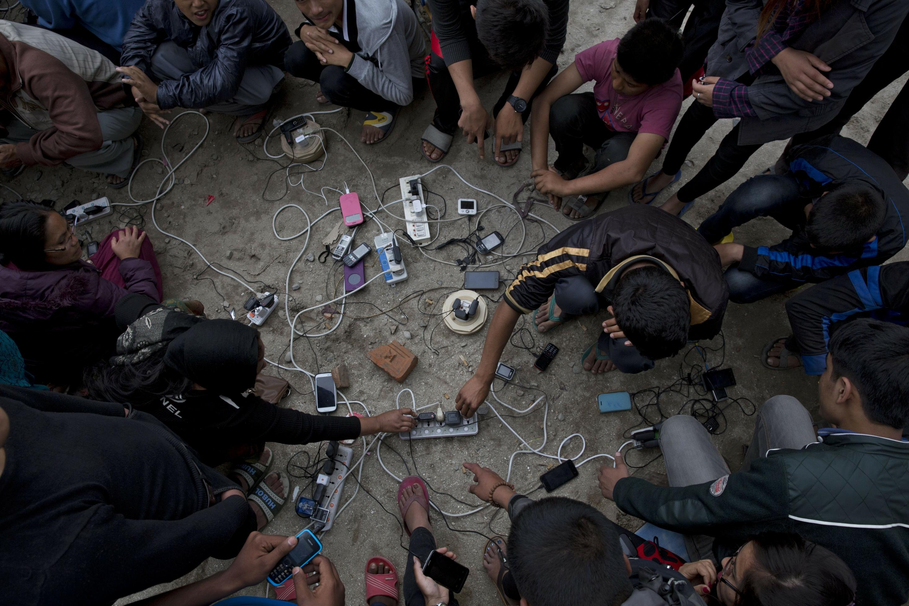 Nach einem Erdbeben im April 2015 luden Dorfbewohner ihre Mobiltelefone auf einer Freifläche in Kathmandu, Nepal. Sie suchten in der erdbebengeschädigten Stadt nach ihren verlorenen Angehörigen.
Das Bild zeigt mehrere Menschen um Handys, die an mehreren Steckern geladen werden.