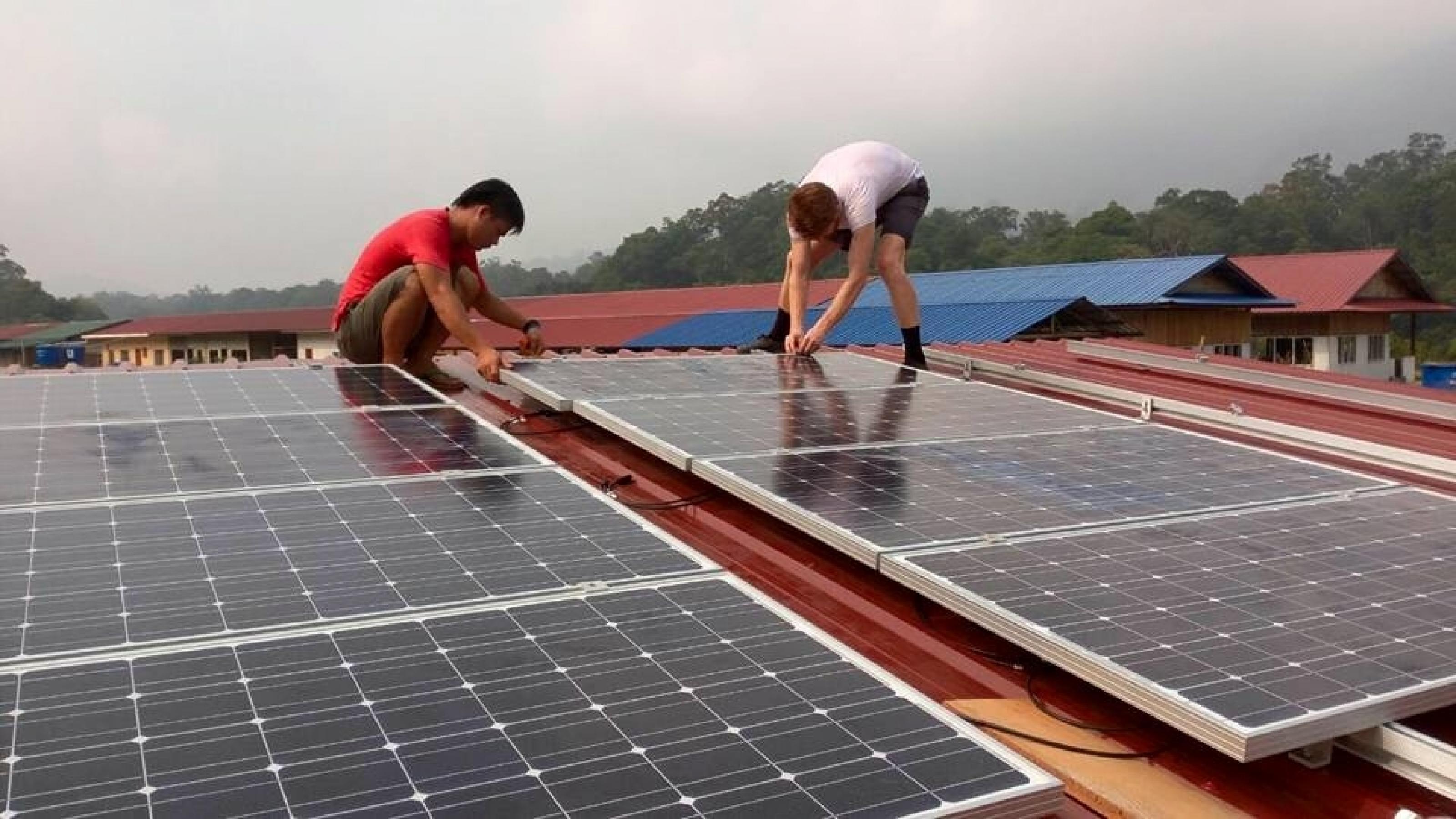 Das Foto zeigt zwei Männer, die Solarzellen auf einem Dach installieren. –
… In manchen Dörfern baut die Firma auch ein Netz auf, in dem das Wasserkraftwerk in der Regenzeit und Solarzellen in der Trockenzeit den Strom liefern. …