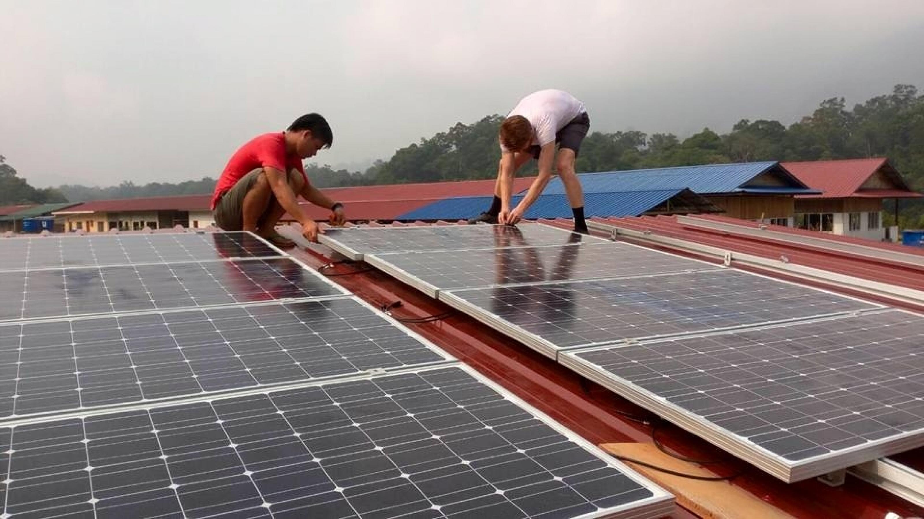 Das Foto zeigt zwei Männer, die Solarzellen auf einem Dach installieren. –
… In manchen Dörfern baut die Firma auch ein Netz auf, in dem das Wasserkraftwerk in der Regenzeit und Solarzellen in der Trockenzeit den Strom liefern. …