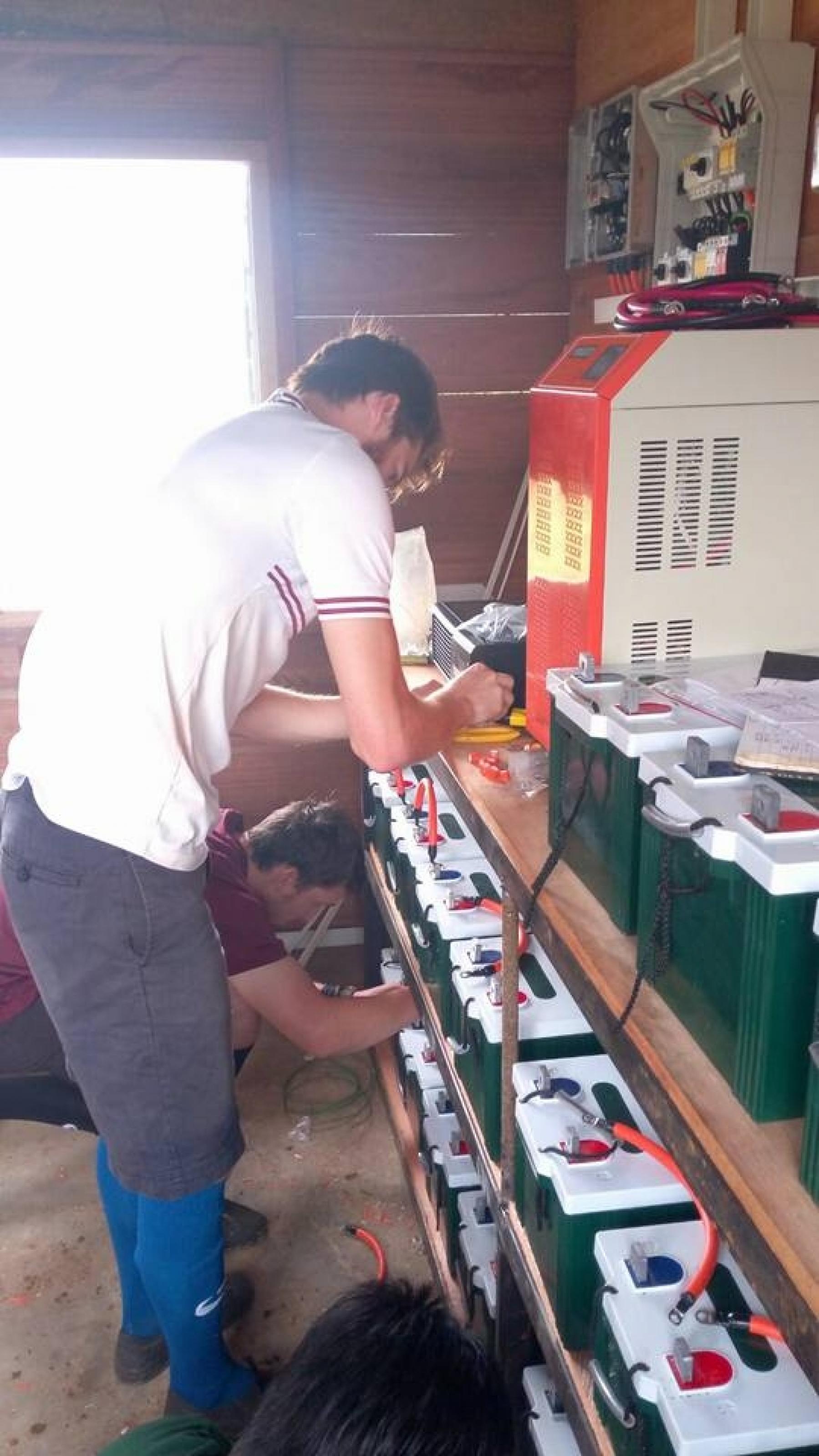 Das Foto zeigt einen Mann, der Batterien in der Größe von Autobatterien mit Kabeln verbindet. –
… Batterien speichern dann den Strom, damit auch nach Sonnenuntergang noch Energie da ist.