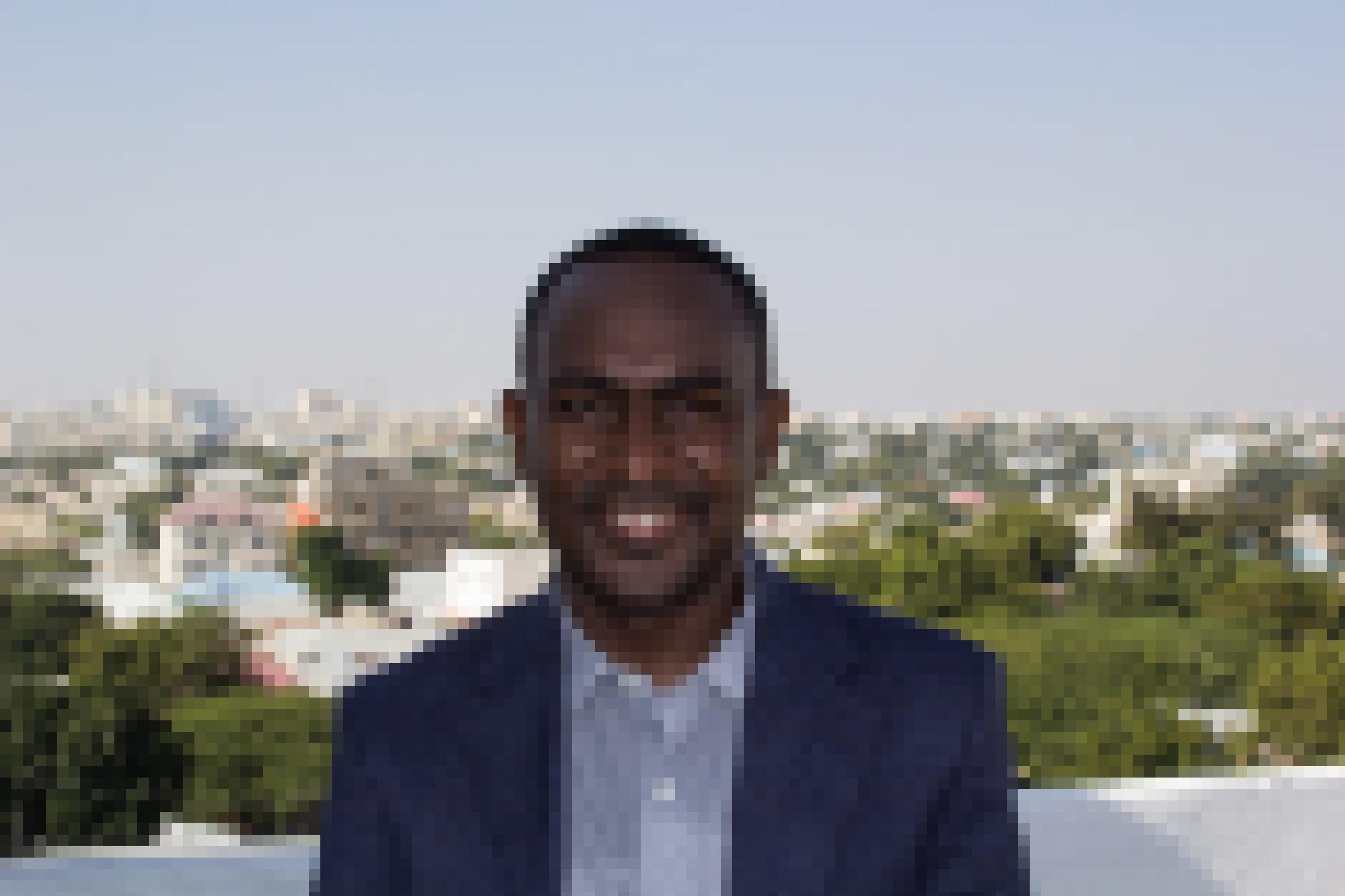 Abdalle Mumin, in Sakko und Hemd, steht auf dem Dach eines Hauses in Mogadischu. Im Hintergrund der Blick über die Stadt.