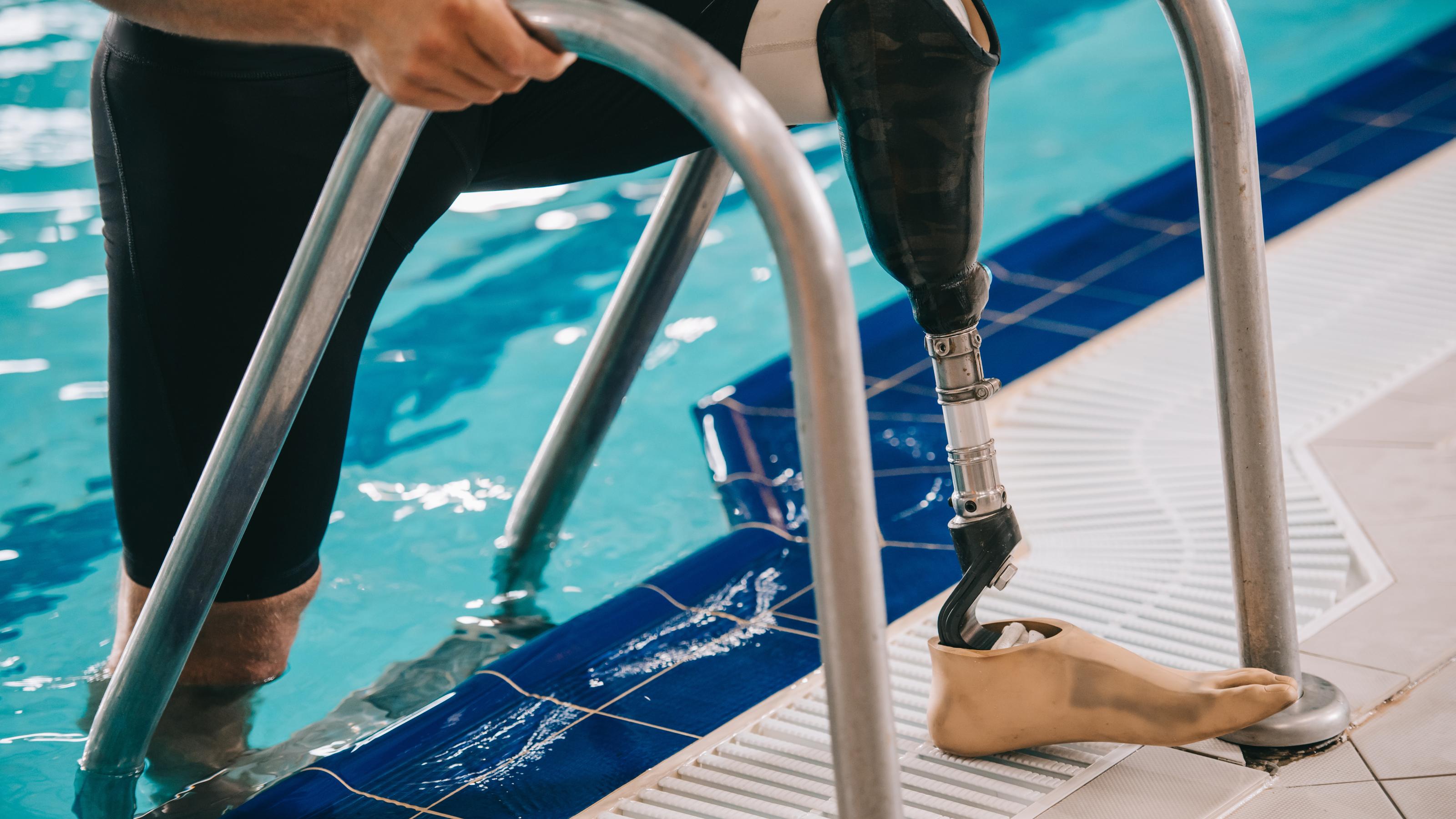 Ein amputierter Mann trägt rechts eine Prothese und steigt gerade über eine Leiter aus einem Schwimmbecken.
