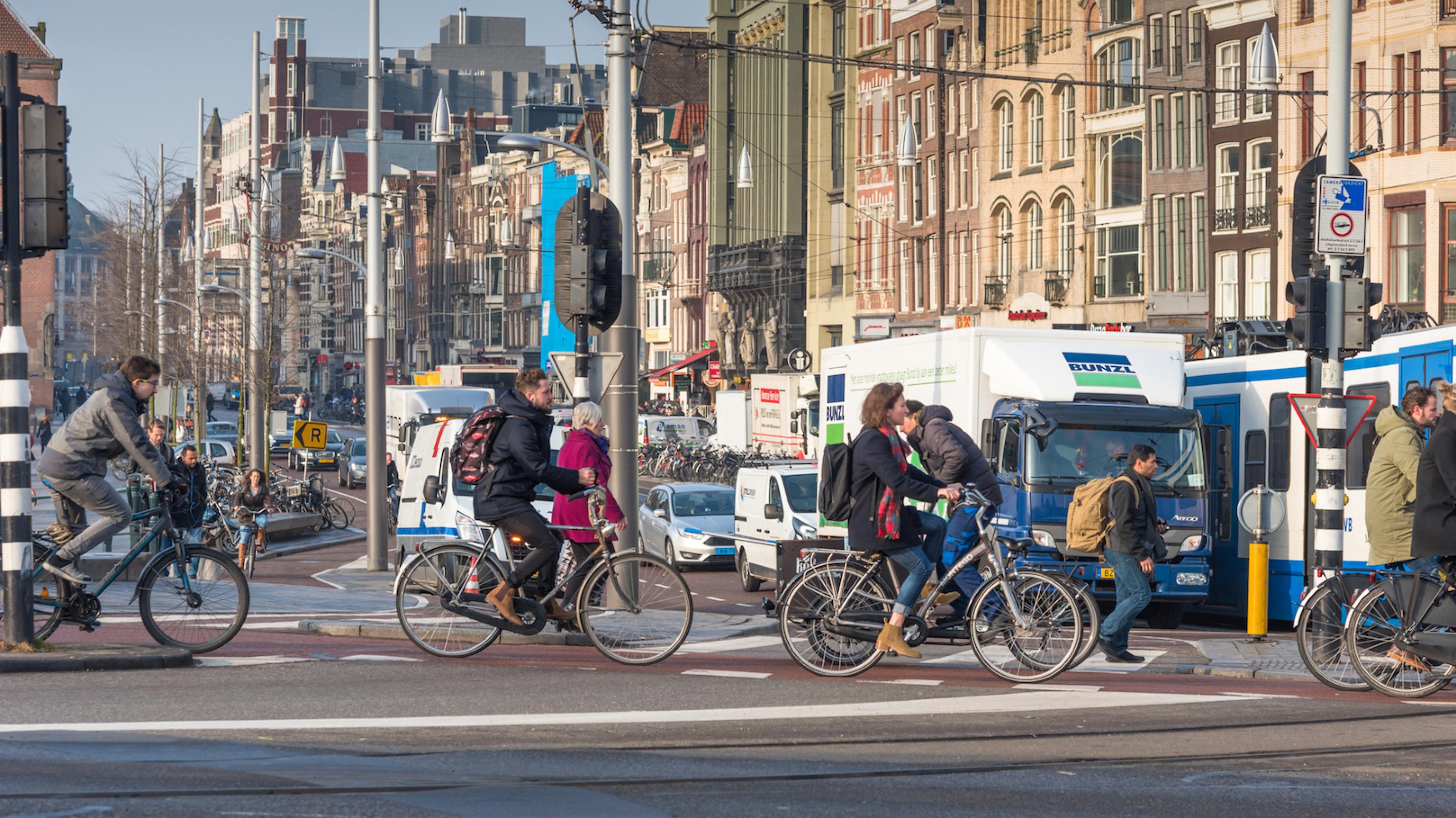 Radfahrer und Fußgänger gehen in Amsterdam über eine stark befahrene Kreuzung