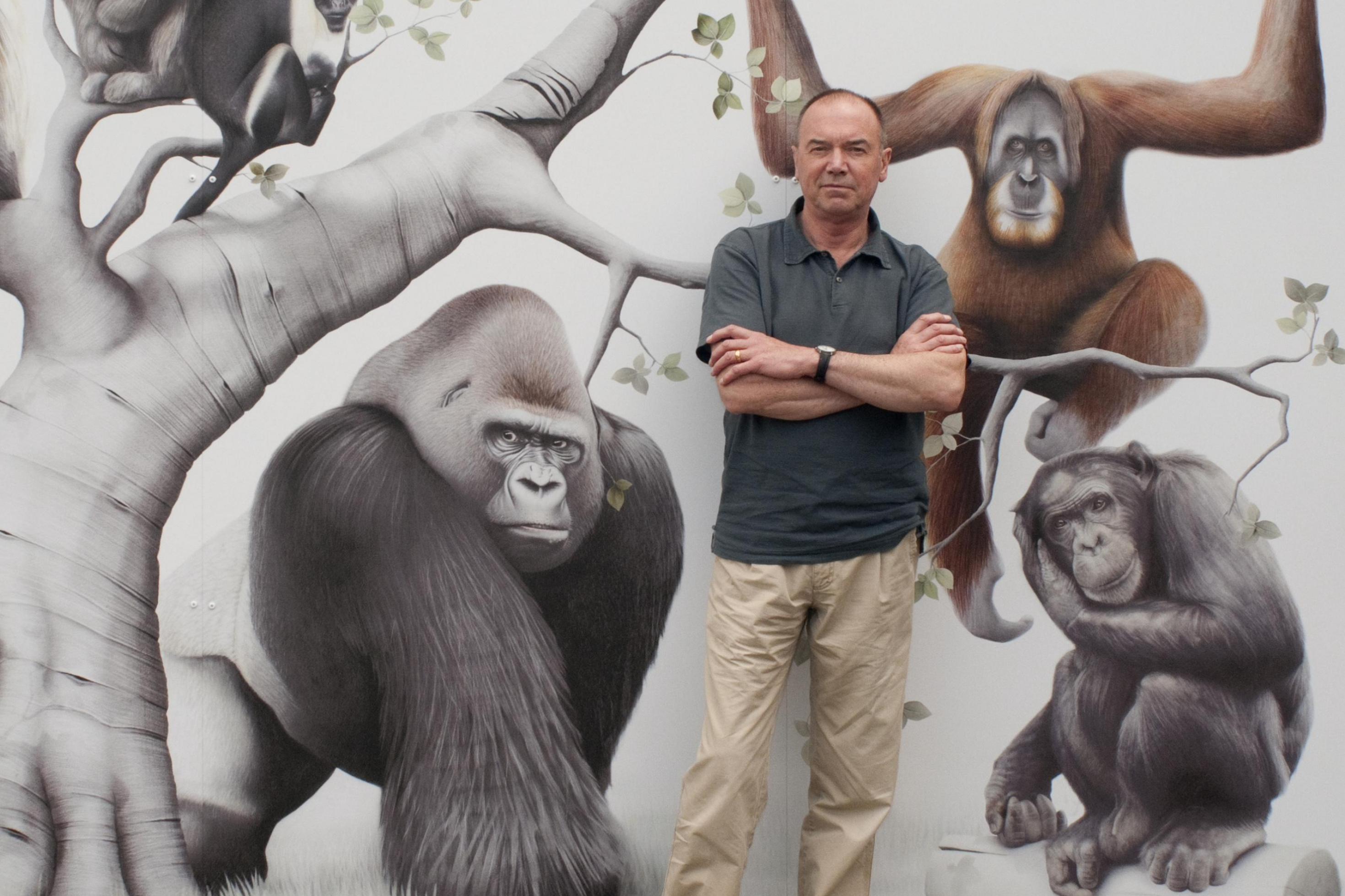 Andrew Whiten, ein schottischer Primatologe, lehnt an einer Wand, auf der mehrere Menschenaffen abgebildet sind.