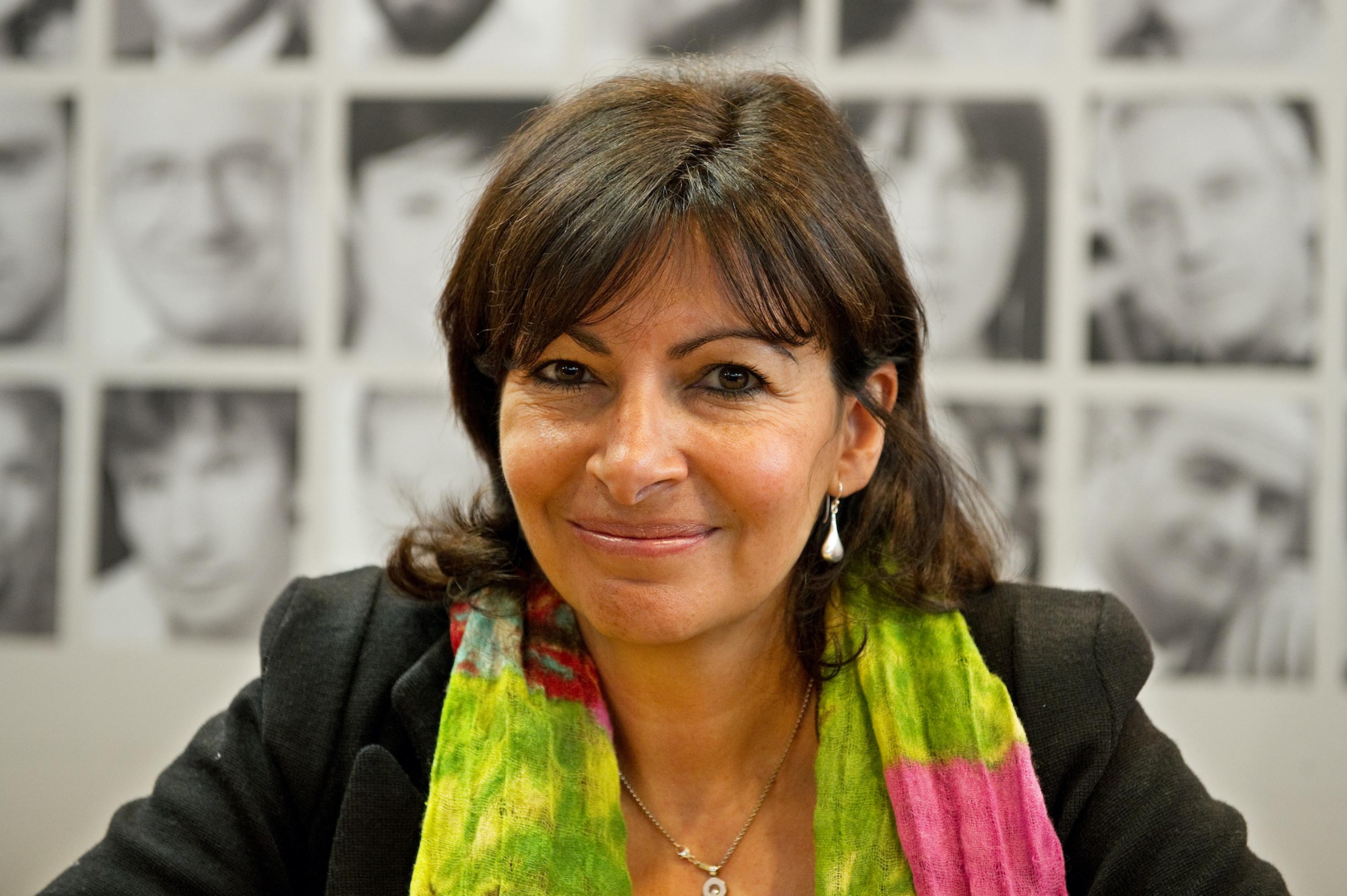 Anne Hidalgo hat glattes, dunkelbraunes schulterlanges Haar. Sie trägt ein schwarzes Jackett und ein buntes Tuch.