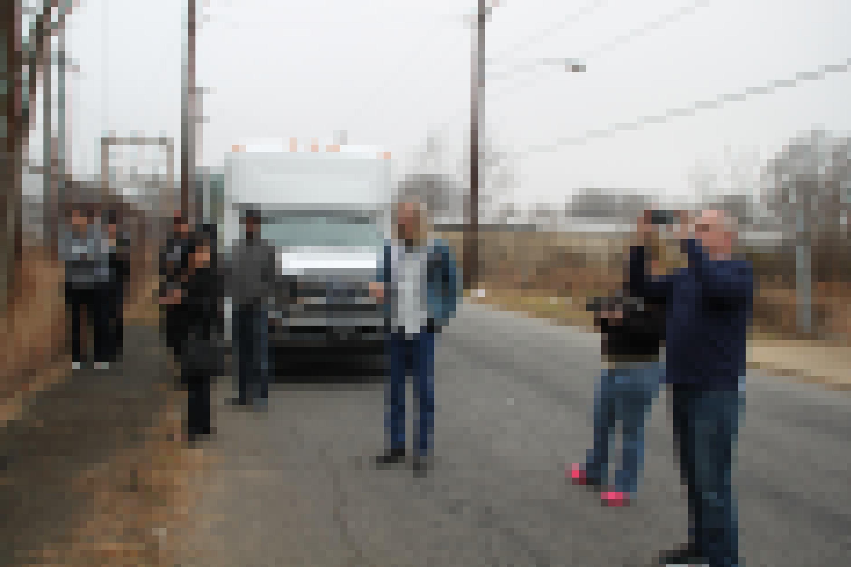 Eine Gruppe von Menschen steht vor einem Kleinbus.