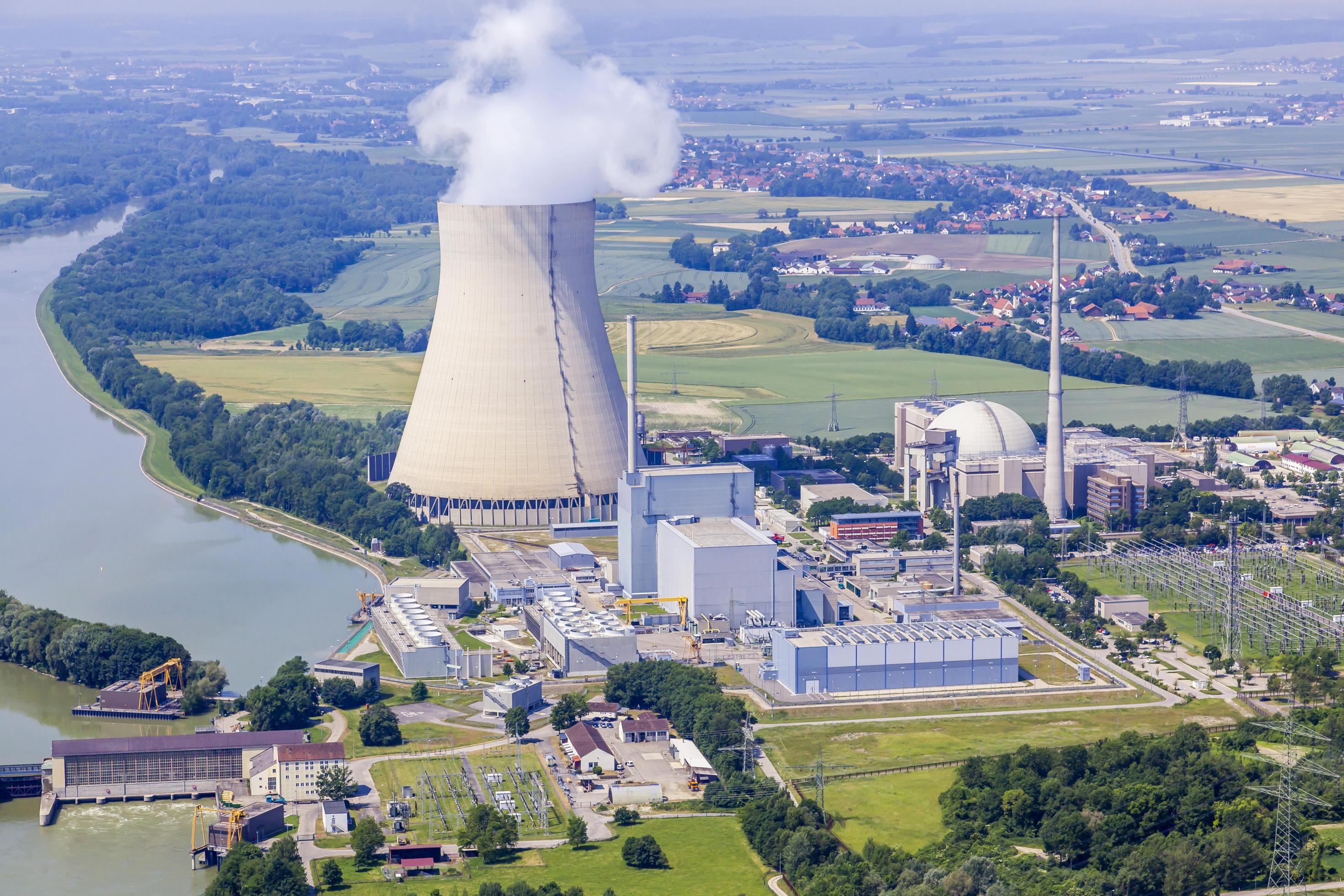 Das Kraftwerk liegt am linken Isarufer bei Essenbach in Niederbayern. Der Kühlturm liegt direkt an einem hier aufgestauten Stück des Flusses, über ihm hängt eine kleine Dampfwolke.