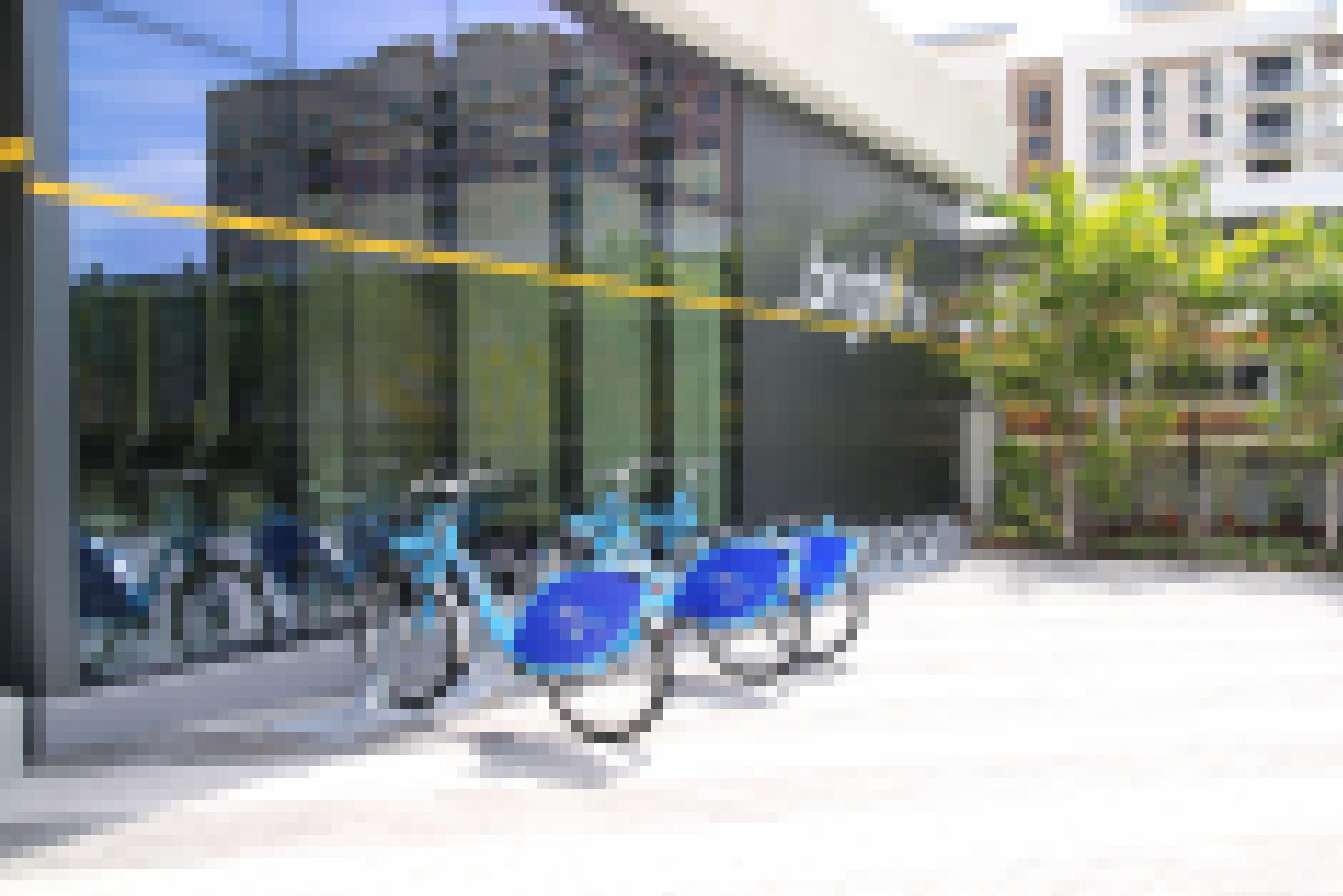 Drei blaue Fahrräder stehen vor einem Gebäude mit Glasfront in Fahrradständern.