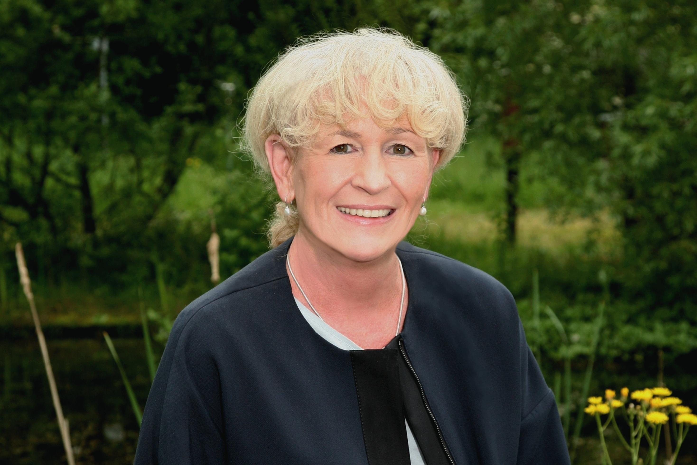 Beate Jessel blickt in die Kamera; im Hintergrund eine Wiese mit Blüten