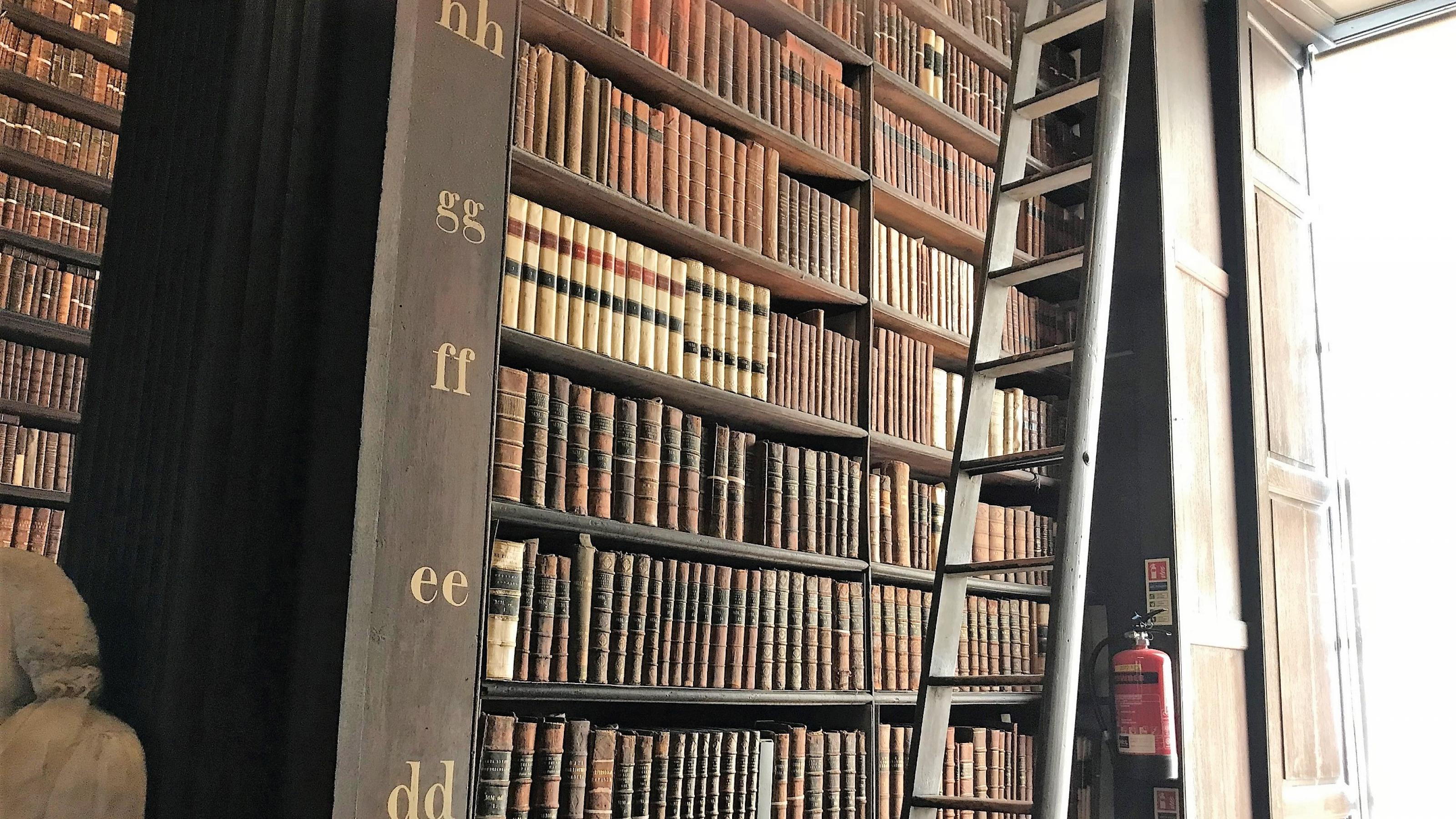 Ein Regal mit vielen alten Büchern der Bibliothek des Trinity College in Dublin, am Rand eine Leiter.