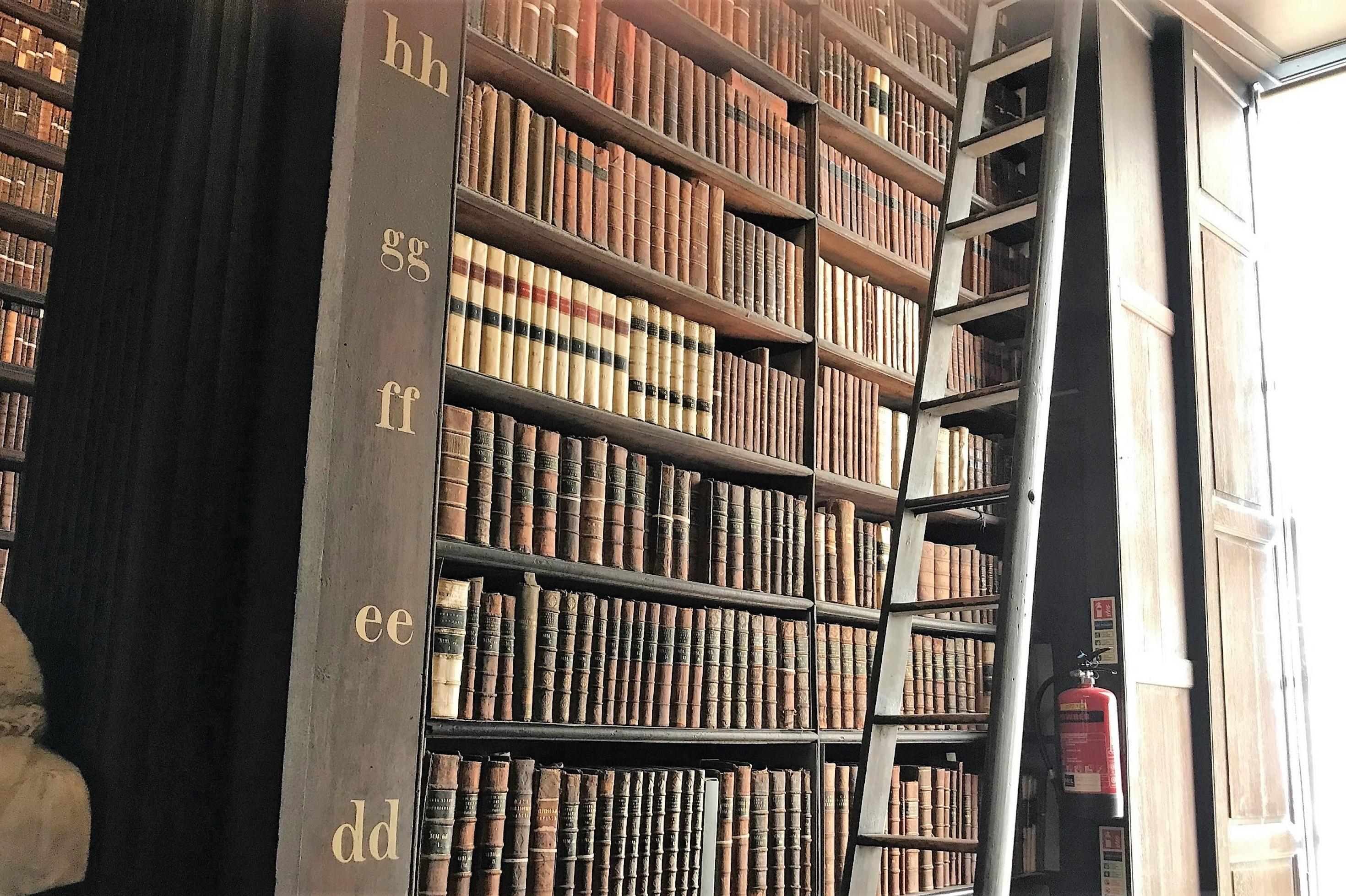 Ein Regal mit vielen alten Büchern der Bibliothek des Trinity College in Dublin, am Rand eine Leiter.