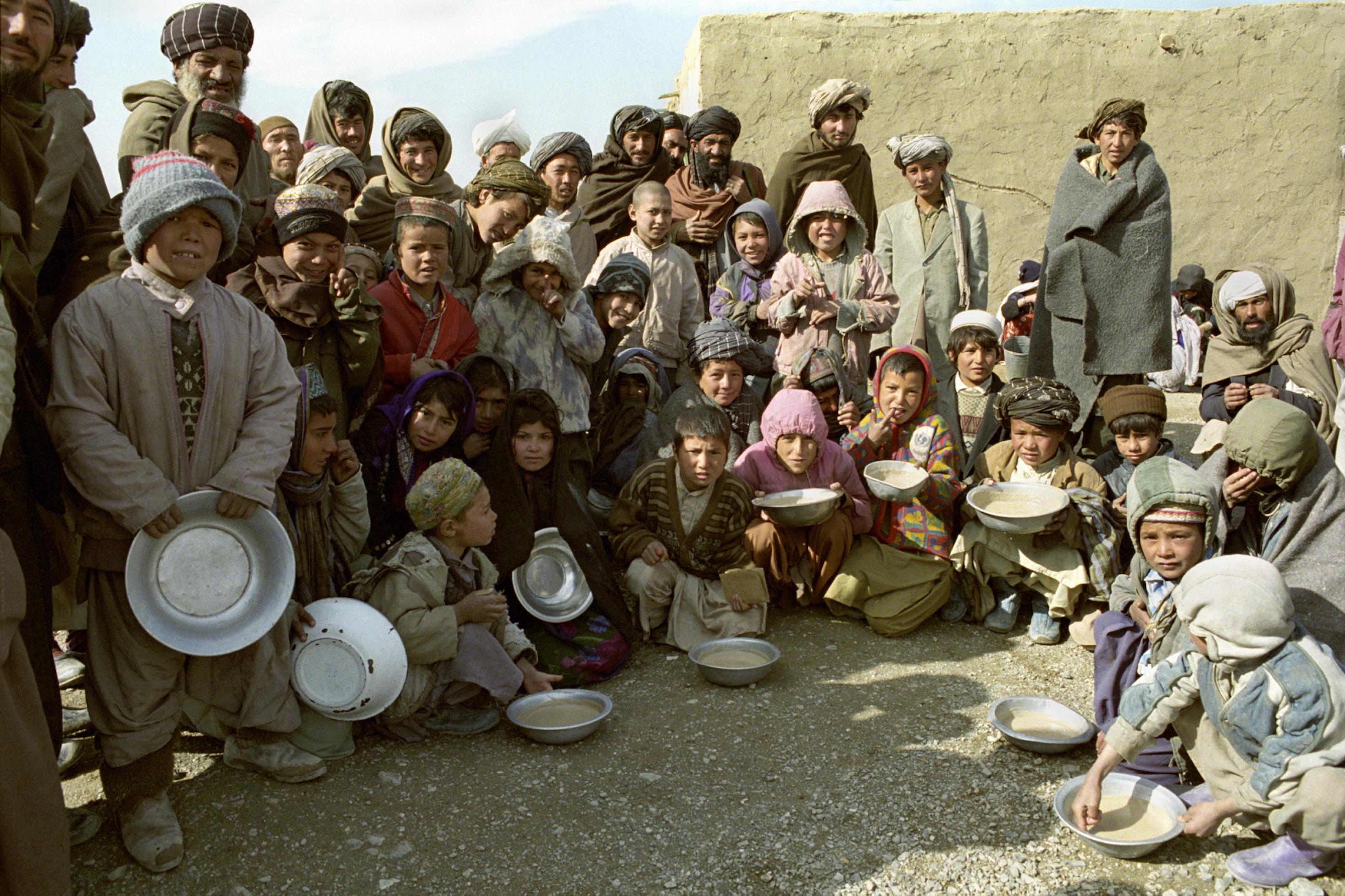 Eine Gruppe von Männern und Kinder, viele mit leeren Schüsseln in der Hand, warten 2002 in Maslakh-Camp in Afghanistan auf Lebensmittel-Hilfe.