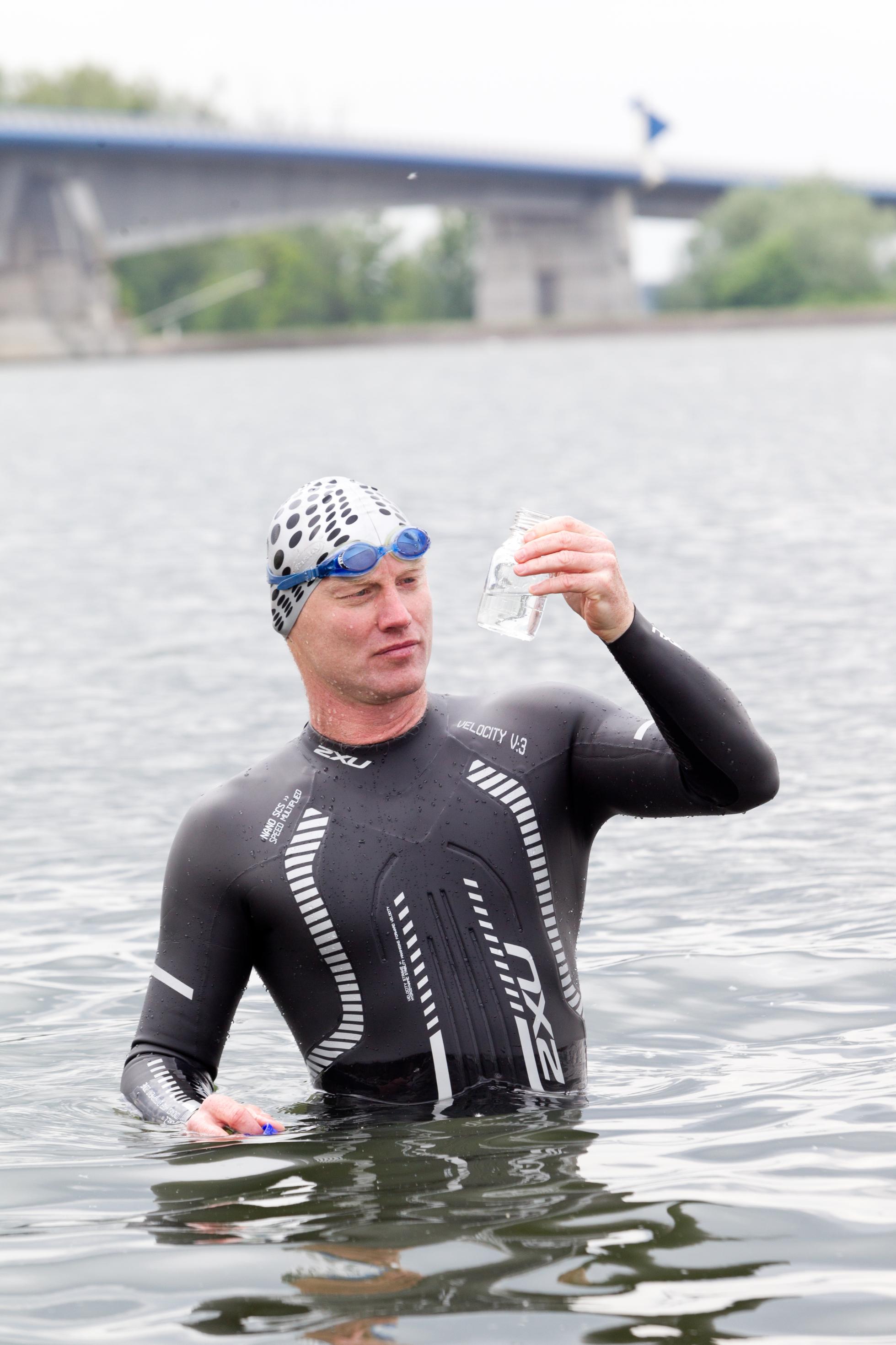 Andreas Fath im Neoprenanzug im Wasser mit Wasserprobe in der Hand