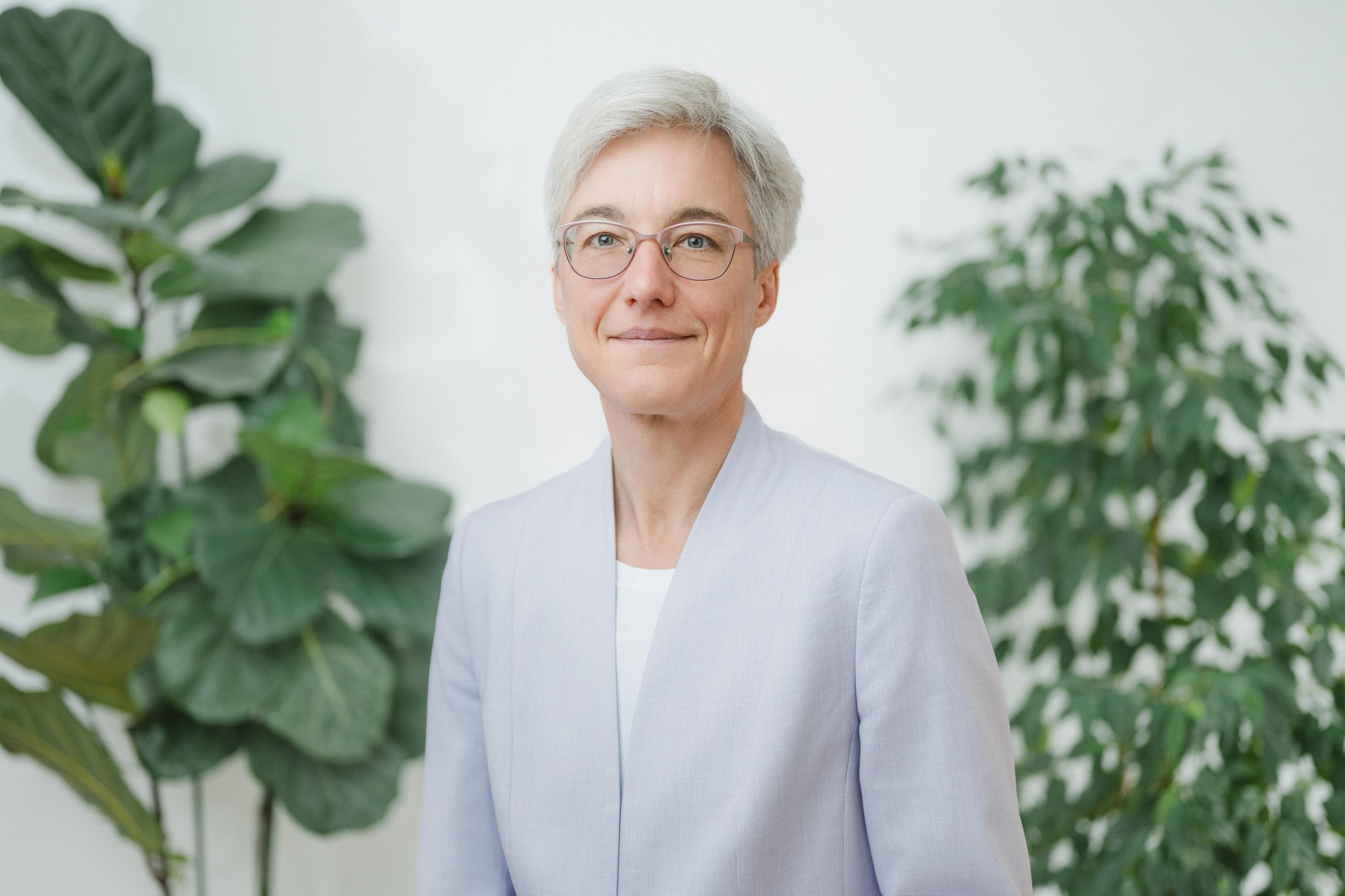 Knopf hat weiße, kurze Haare und trägt eine Brille. Im Hintergrund der Portaitaufnahme sieht man zwei Zimmerpflanzen.