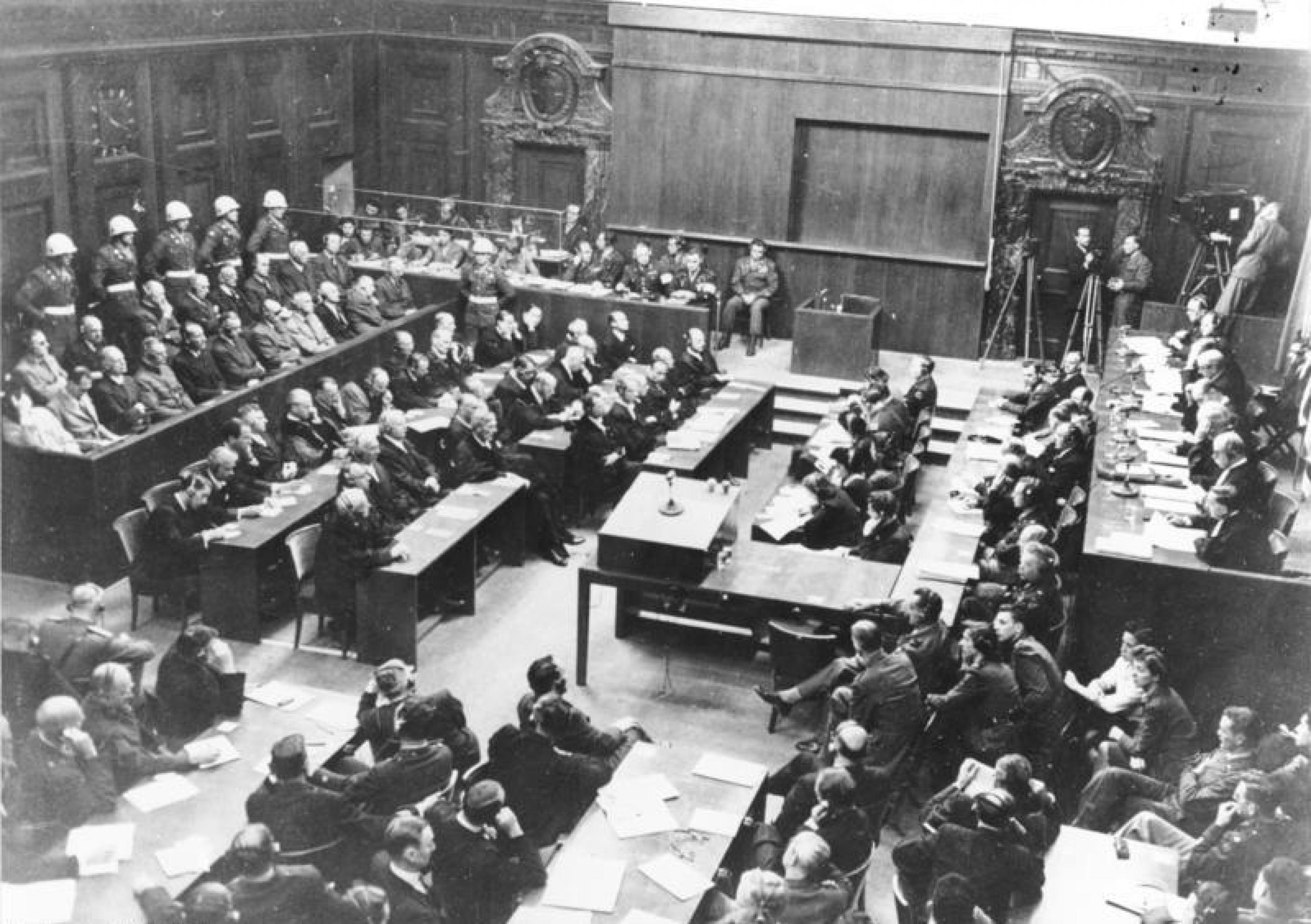 Das Schwarzweiß-Bild zeigt au der Vogelperspektive einen Gerichtssaal. Links sind die Angeklagten zu sehen, rechts die Richterbank.