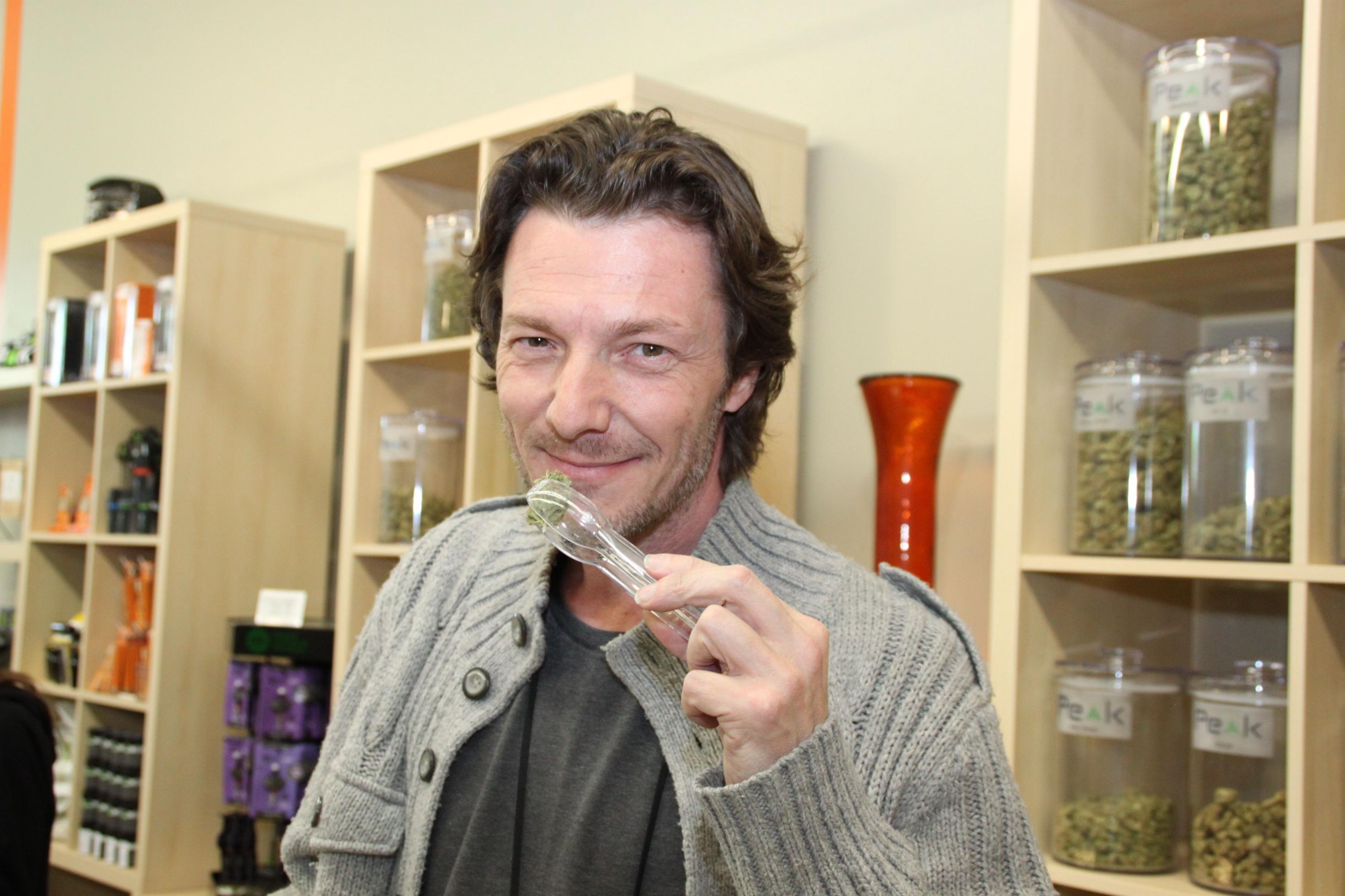 Ein Mann mittleren Alters hält Marihuana-Blüten in einer Zange.