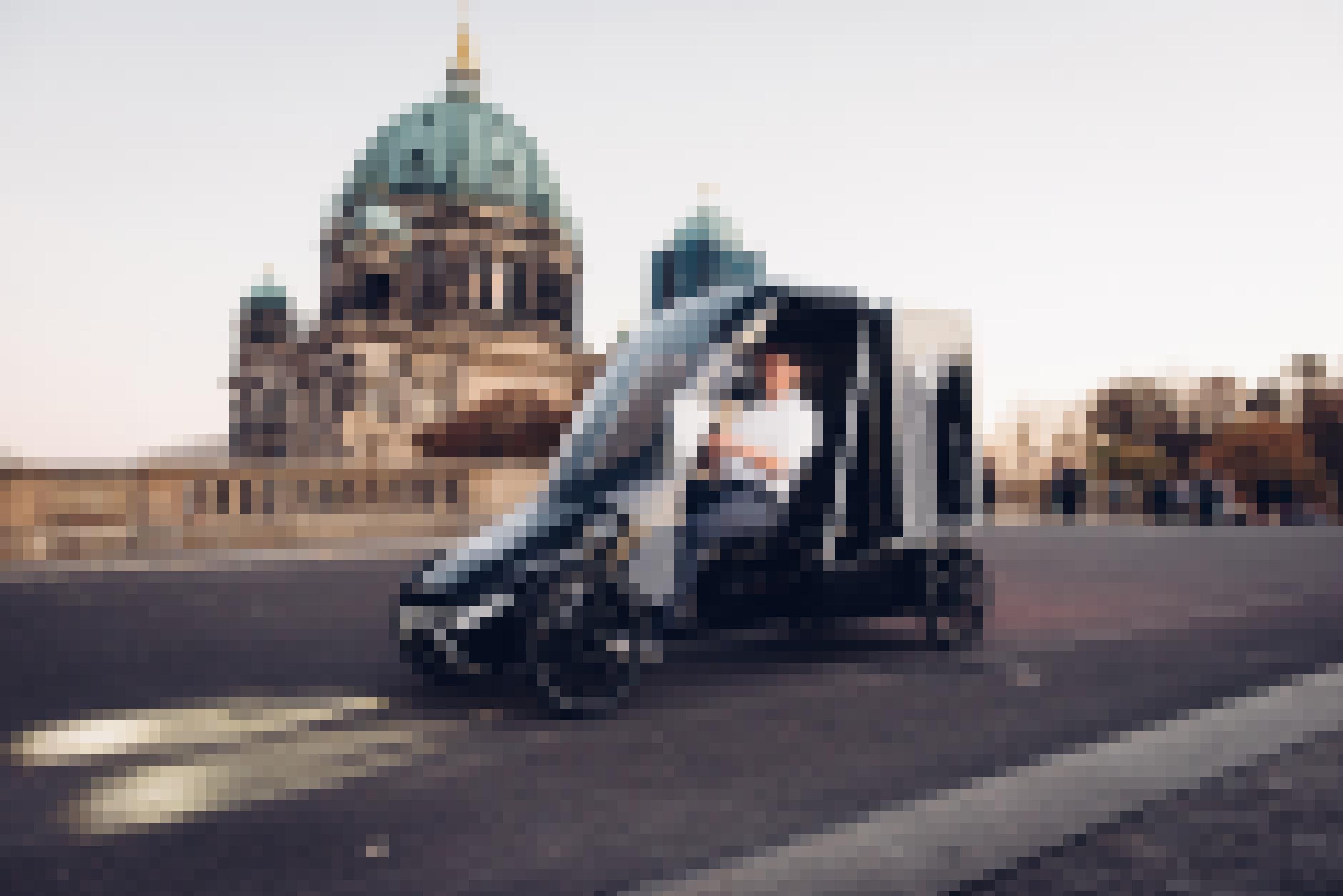 Das schwarzfarbene Citkar ist wie ein Kettcar gebaut. Hat aber eine menschenhohe Fahrerkabine und dahinter einen ebenso hohen Aufsatz. Der Fahrer trägt ein weißes Hemd und fährt mit dem Citkar über eine Straße. Im Hintergrund befindet sich ein historisches Gebäude mit einer Kuppel.
