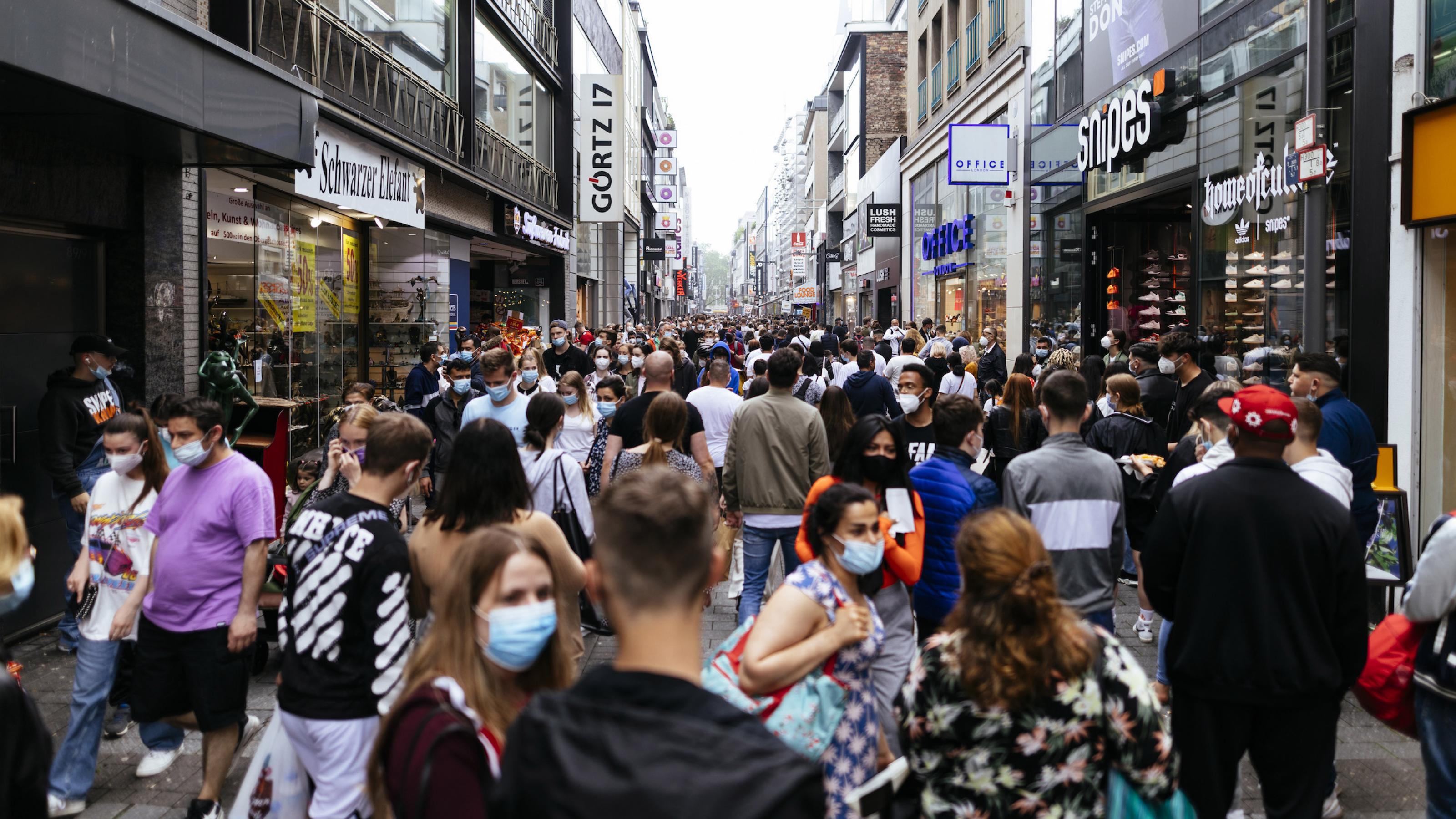 Menschen drängen sich beim Einkaufen in einer typischen deutschen Fußgängerzone. Einige tragen Gesichtsmasken zum Schutz vor einer Coronainfektion.