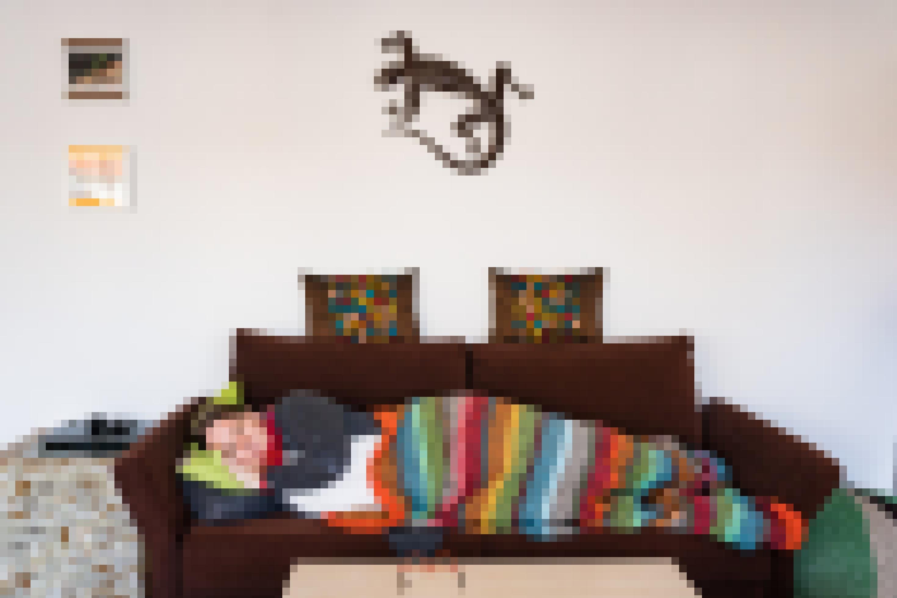 Eine junge Frau liegt in eine bunte Decke gehüllt auf ihrem Sofa und schaut erschöpft an der Kamera vorbei.
