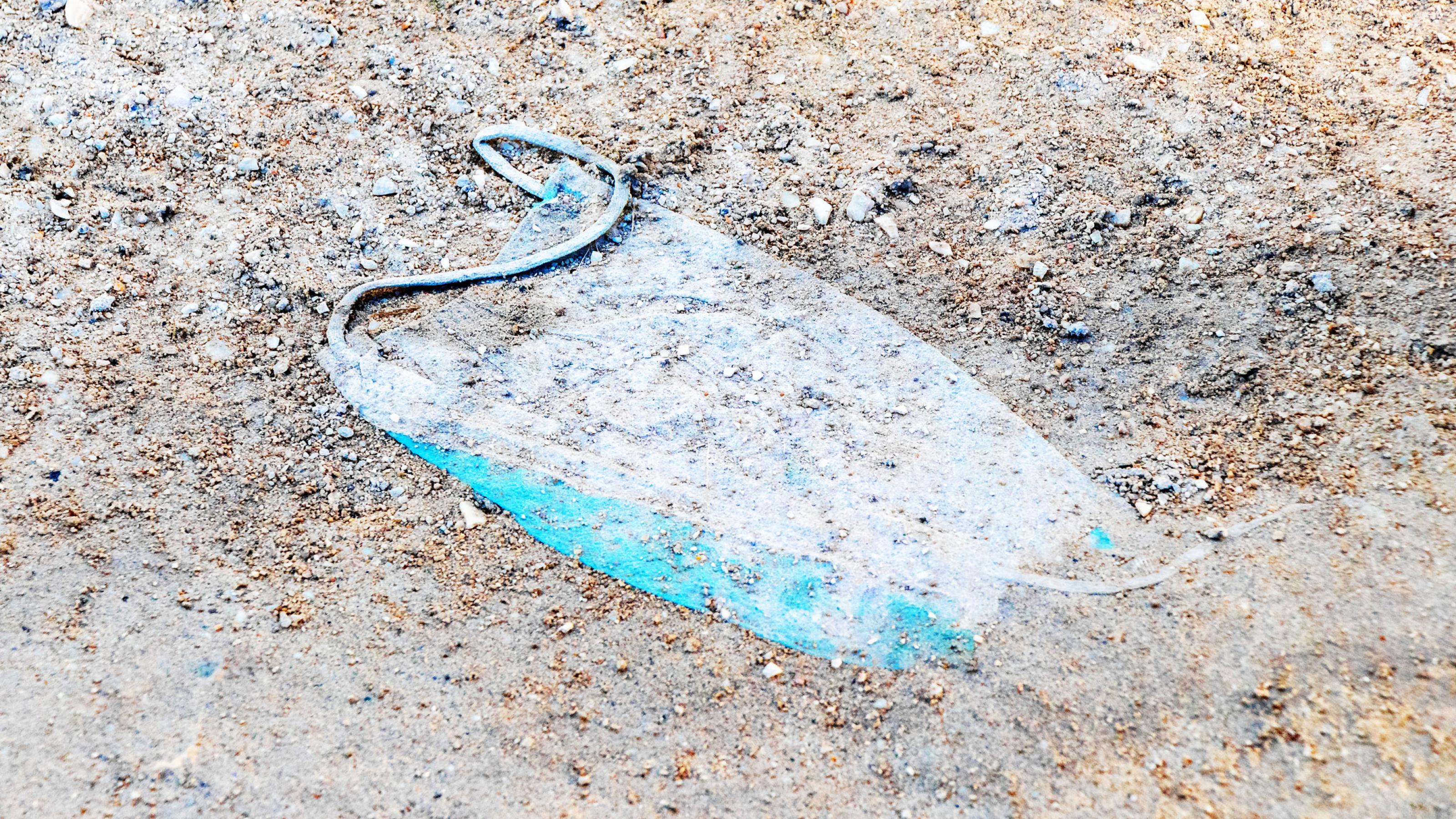 Eine gebrauchte medizinische Corona-Schutzmaske liegt auf einem Sandboden im Dreck.
