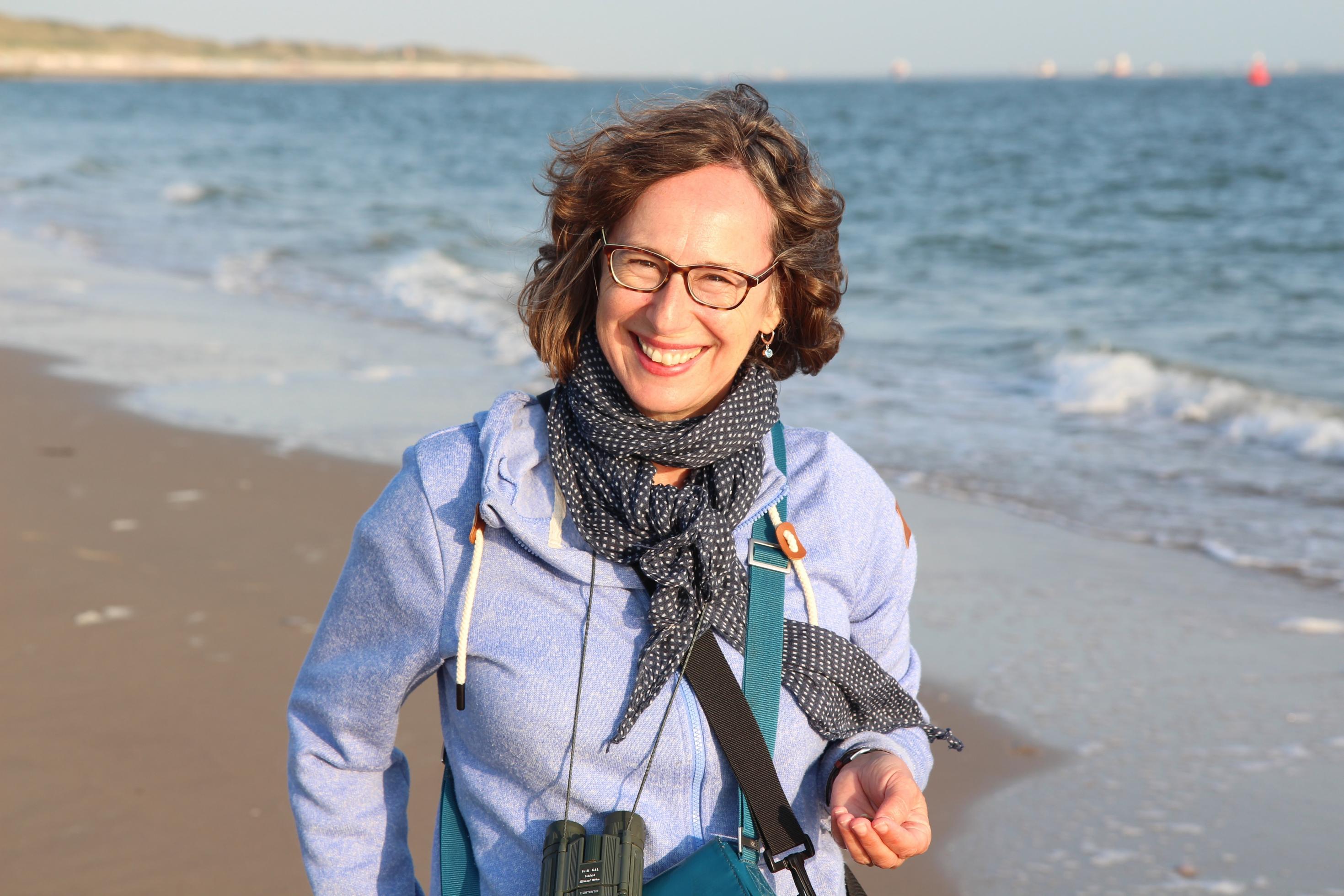 Daniela Pauli an einem Strand. Sie trägt ein Fernglas um den Hals.