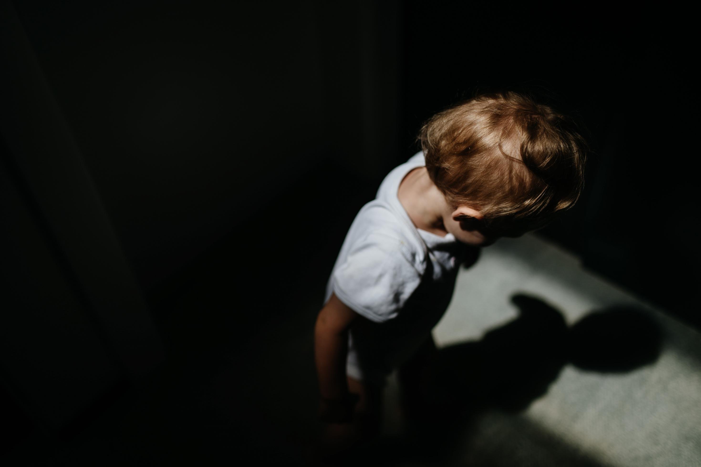 Symbolbild: Ein einsames, anonymisiertes Kind steht in einem dunklen Raum.