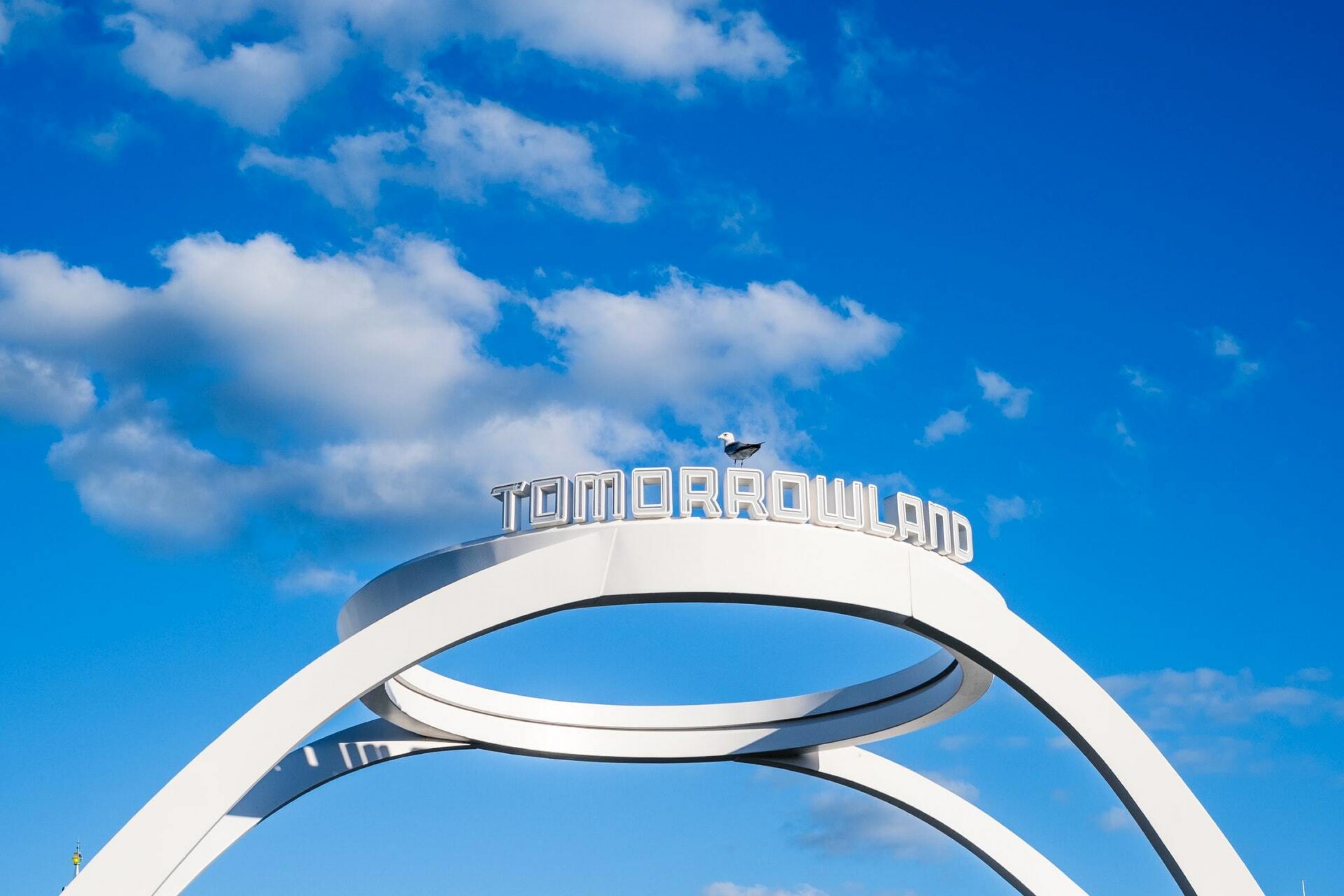 Ein Bogen mit dem Schriftzug Tomorrowland vor blauem Himmel, Eingang zur Attraktion unter anderem mit Mondrakete, Freeways und Monorail