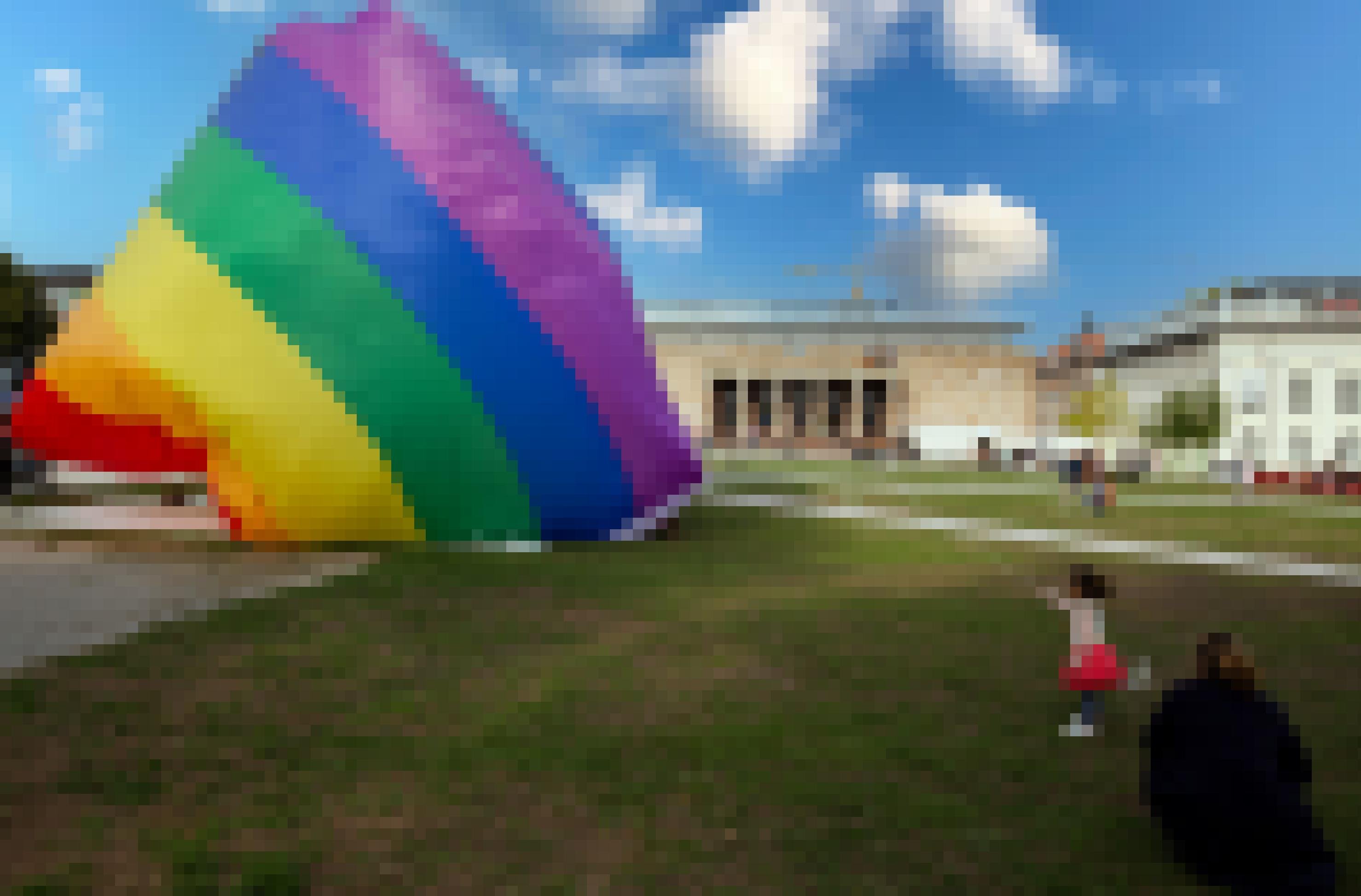 Kind hält einen riesigen Balon in Regenbogenfarben in der Hand.