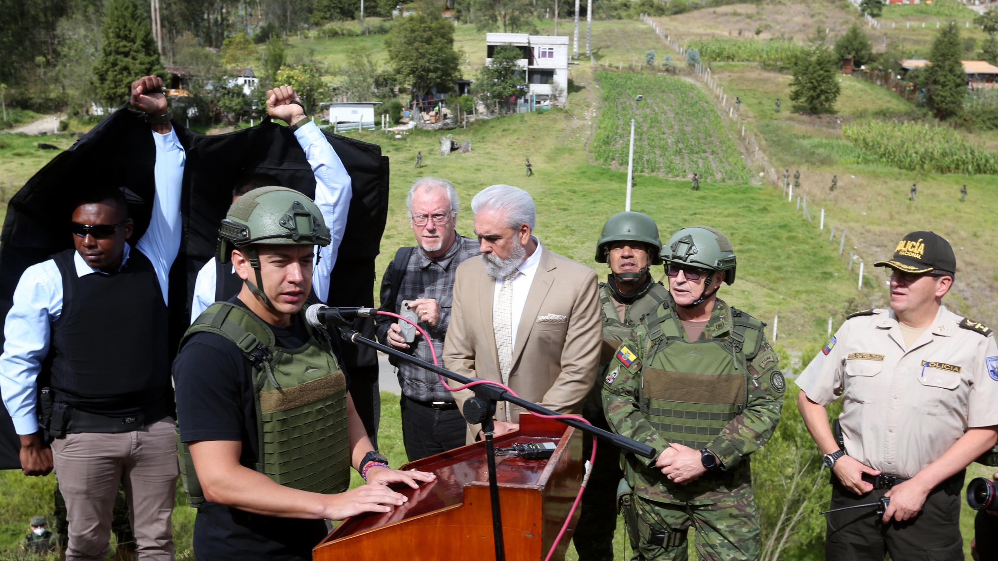 Ecuadors Präsident Daniel Noboa mit kugelsicherer Weste und Helm an einem Rednerpult, umgeben von Militärs.