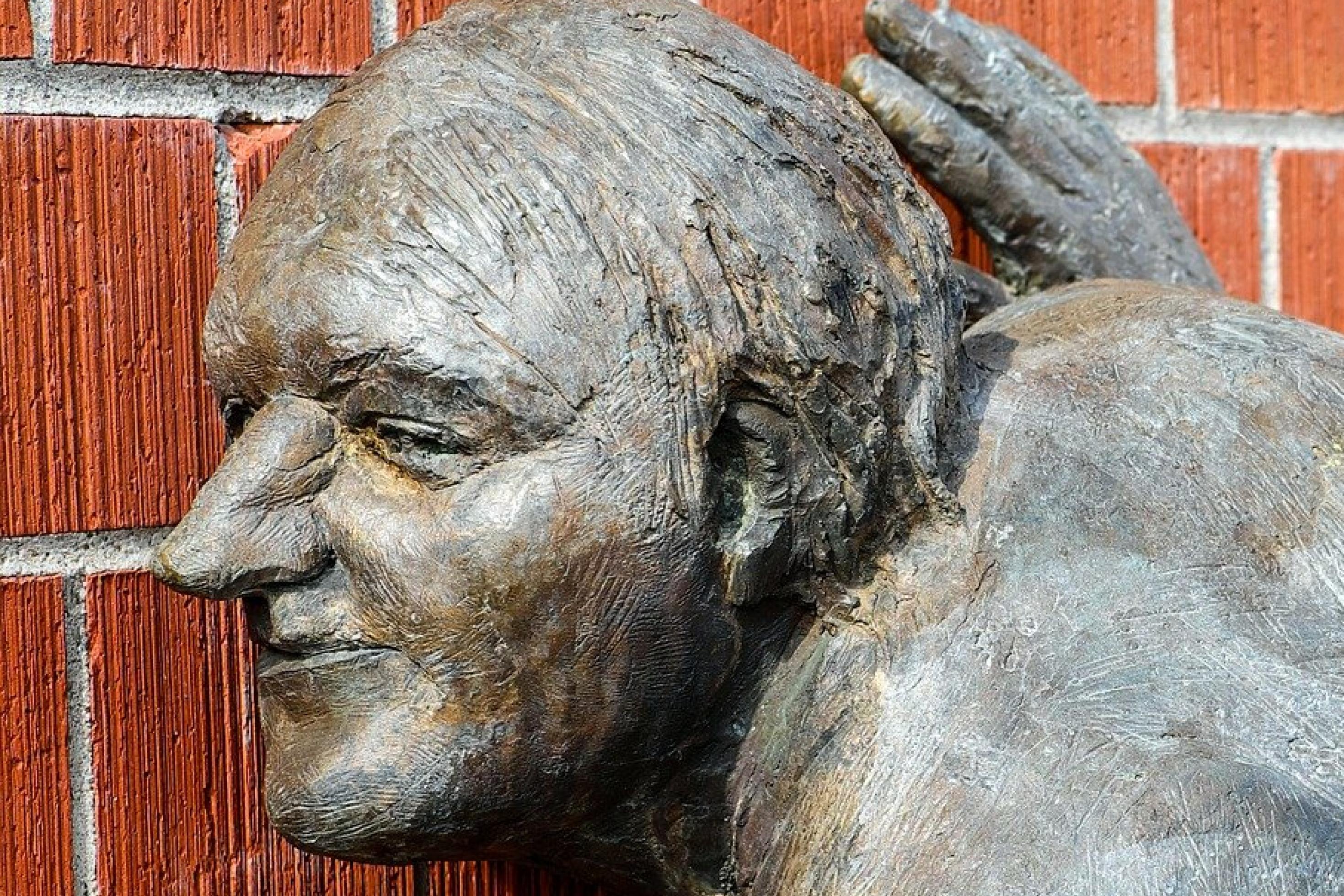 Skulptur eines Lauschers, der sein Ohr an eine Mauer legt.