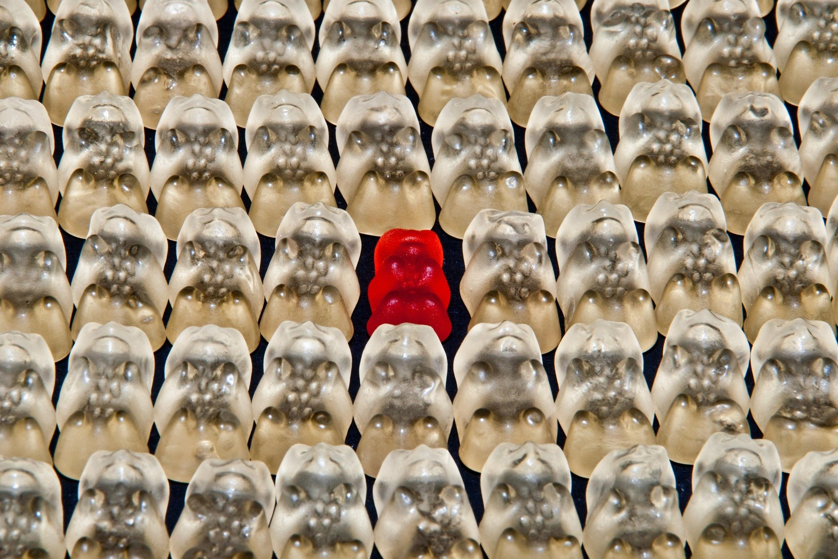 Rotes Gummibärchen umgeben von vielen weißen als Symbol für Individualität