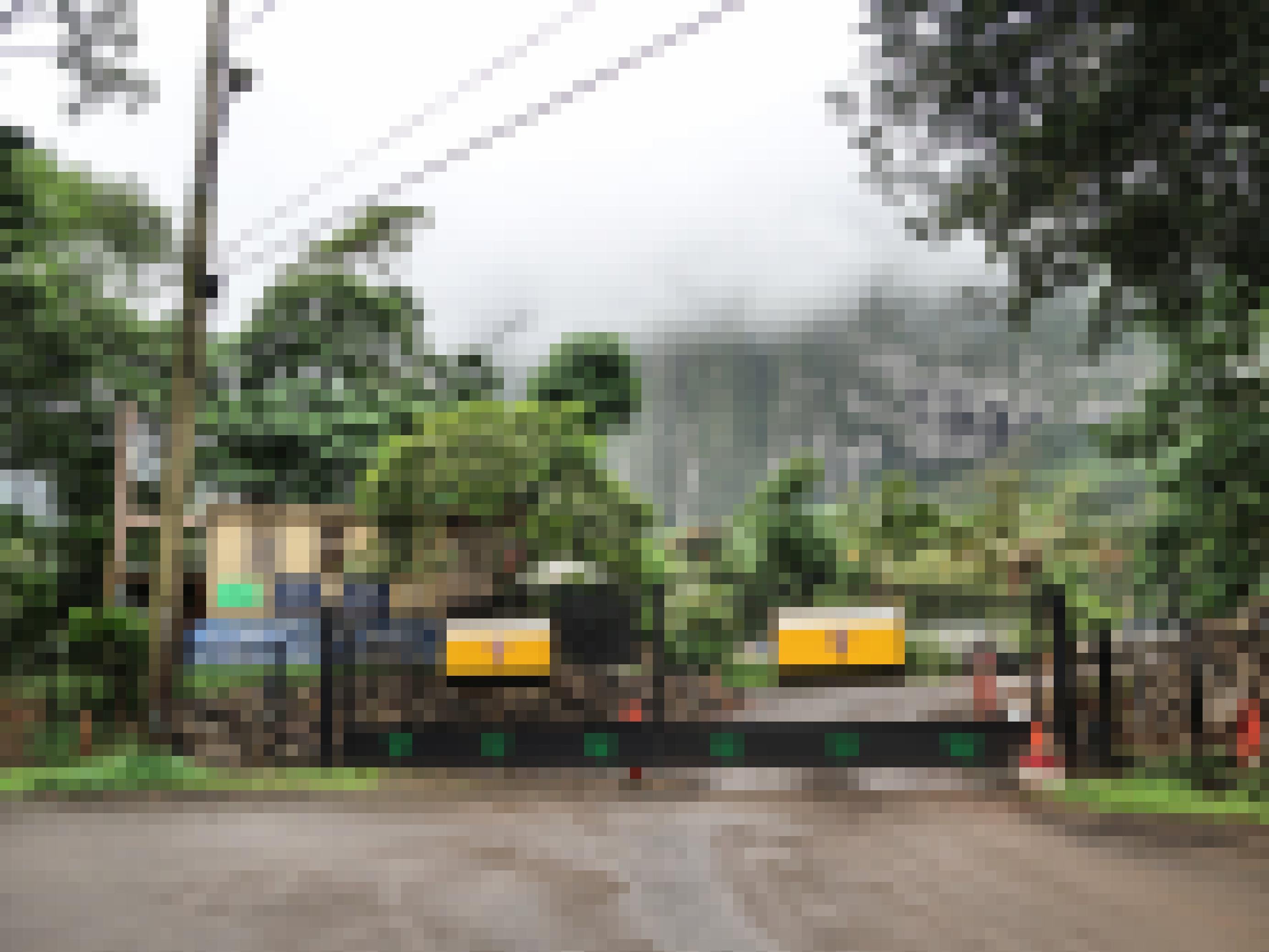 Ein geschlossenes Tor vor einem tropischen, bergigen Gelände. Im Hintergrund ist Nebel zu sehen.