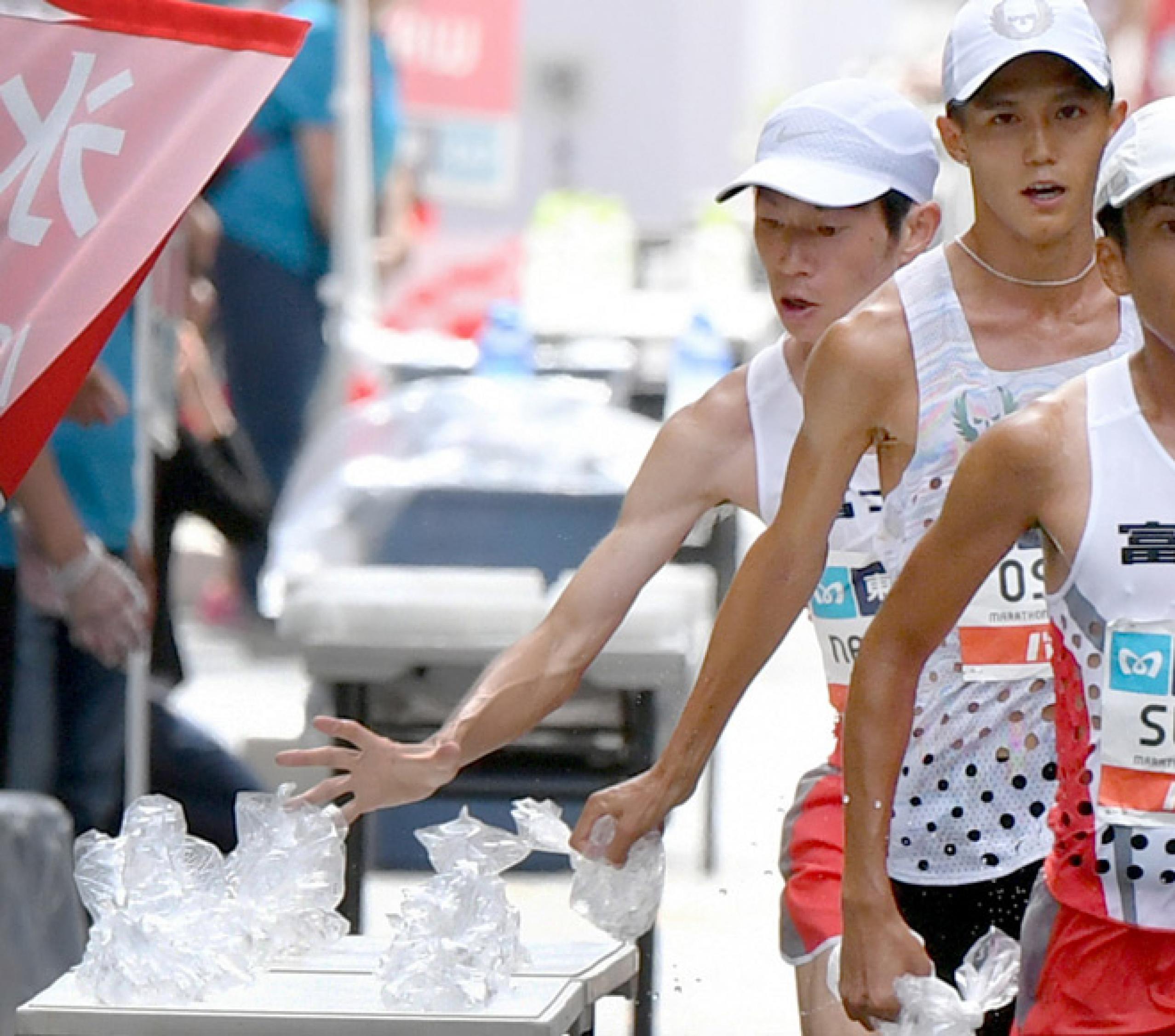 Drei Männer laufen an einem Tisch vorbei, der hinterste greift gerade nach einem Beutel. Bei der Marathon-Meisterschaft in Tokio (September 2019) brauchen die Läufer Kühlung in Form von bereitgestellten Tüten mit Eiswürfeln.