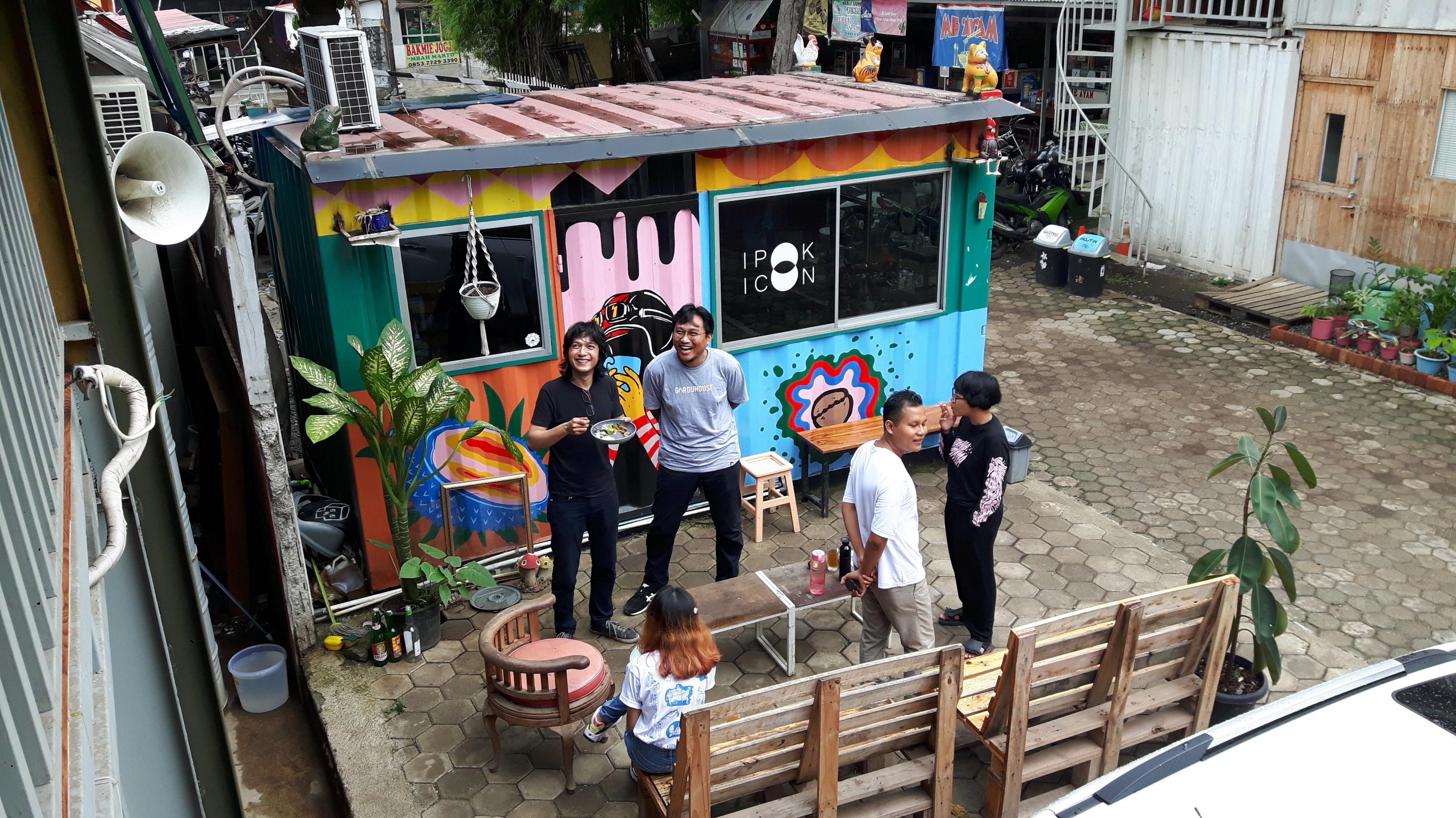 Fünf Personen stehen und sitzen vor dem bunten Pförtnerhaus des Gudskul „Studienkollektiv und Ekosystem für zeitgenössische Kunst“ von ruangrupa in Jakarta