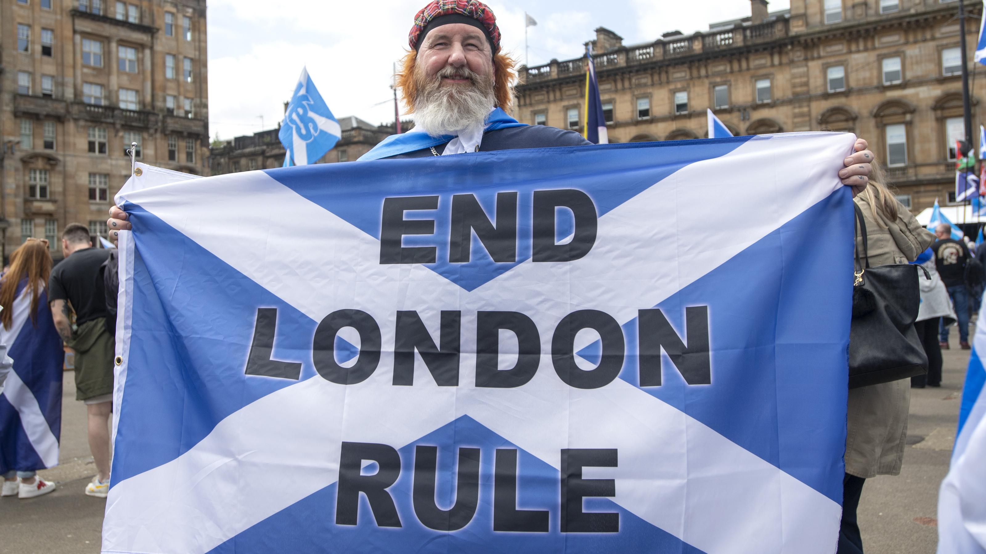 Ein Protestierender ist zu sehen, er hält eine Flagge hoch, auf der steht: End London Rule